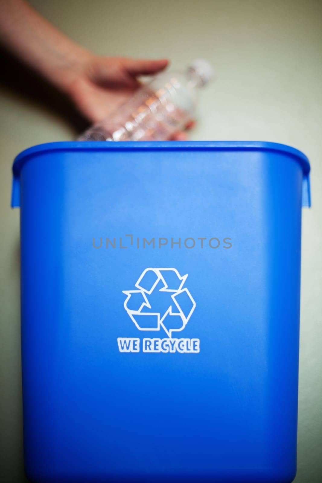 Woman's arm dropping plastic bottling into recycling container