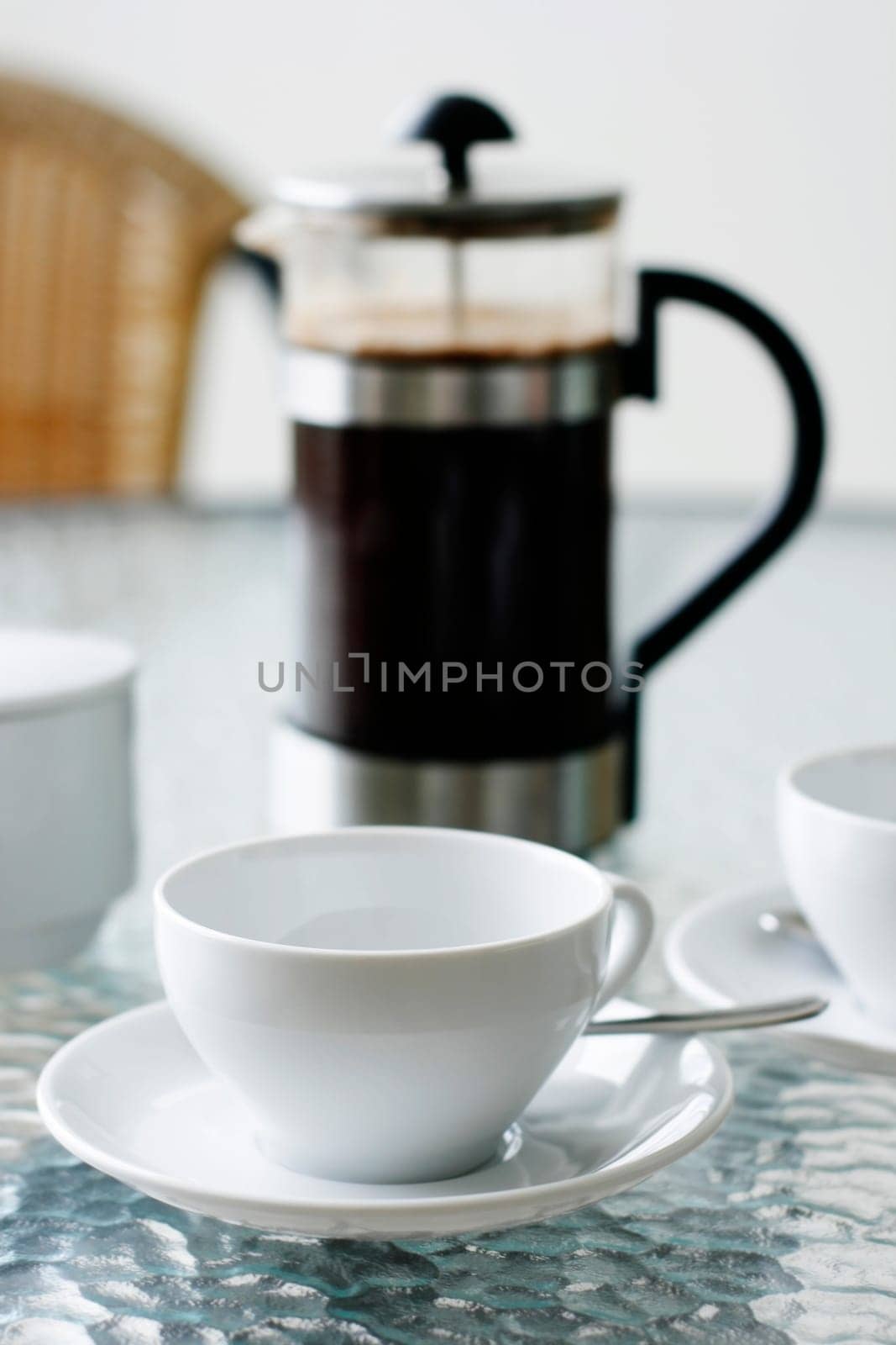 A black filter coffee in a white cup with a coffee plunger in the background on a glass table.