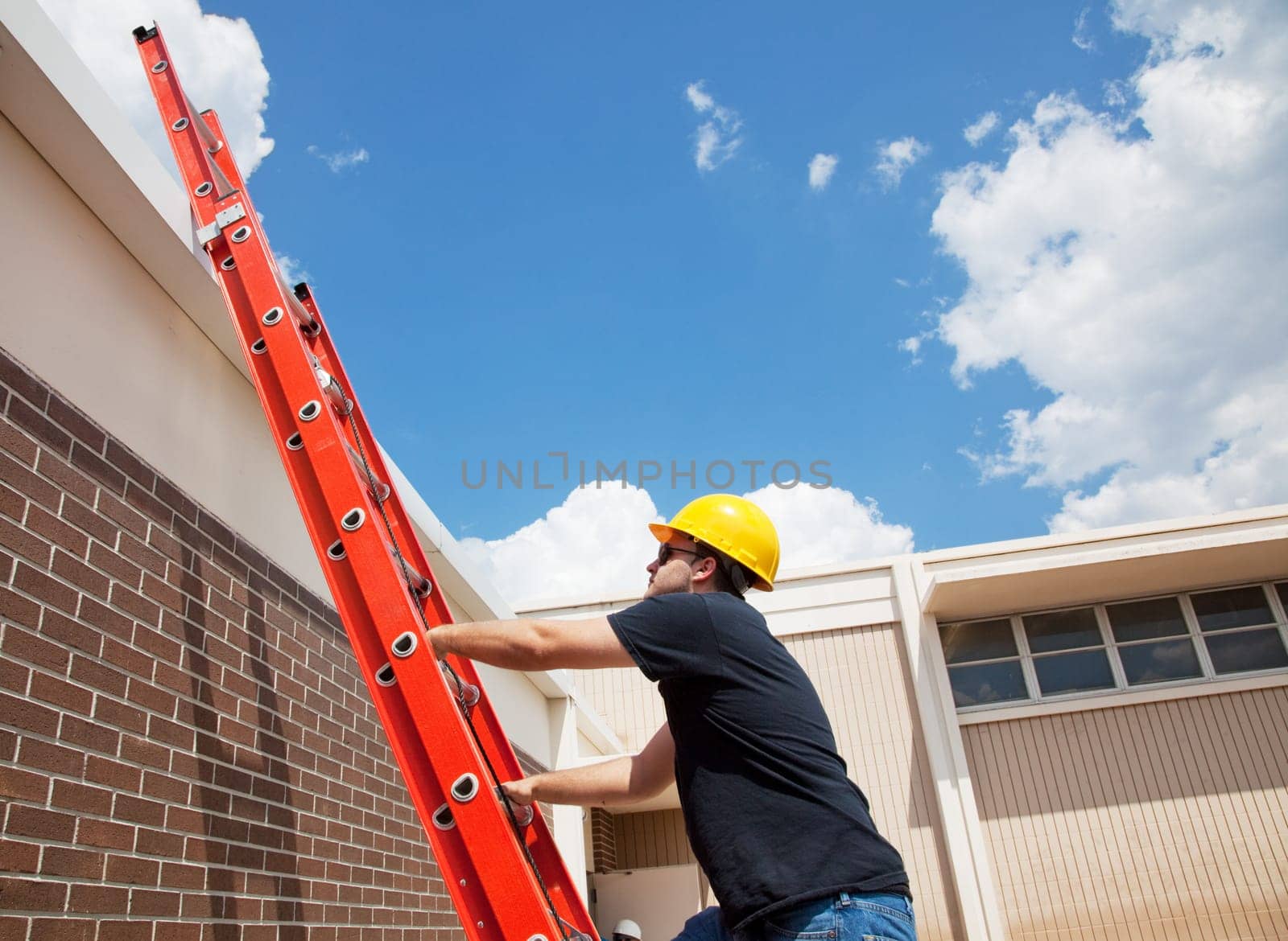Construction worker climbing up to the roof of a building.  Wide view with lots of room for text.