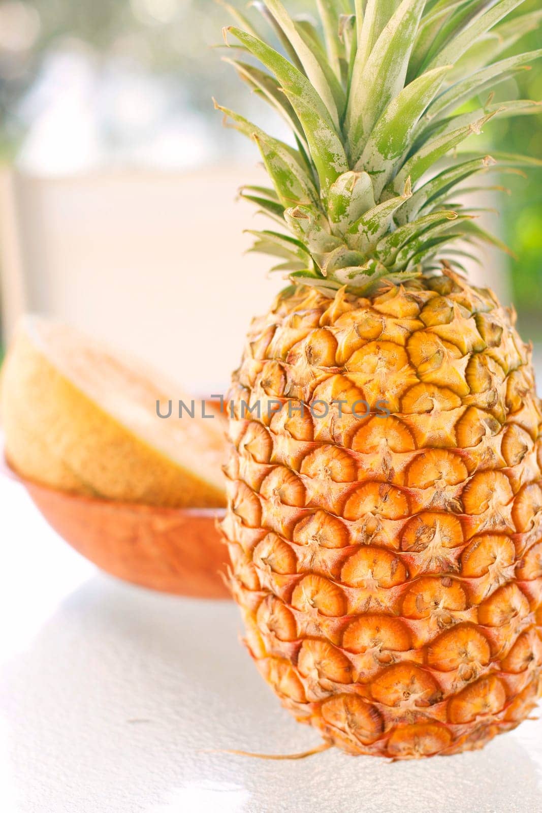 A colorful arrangement of tropical fruit on a glass table with a pineapple and rockmelon as the main items of focus.
