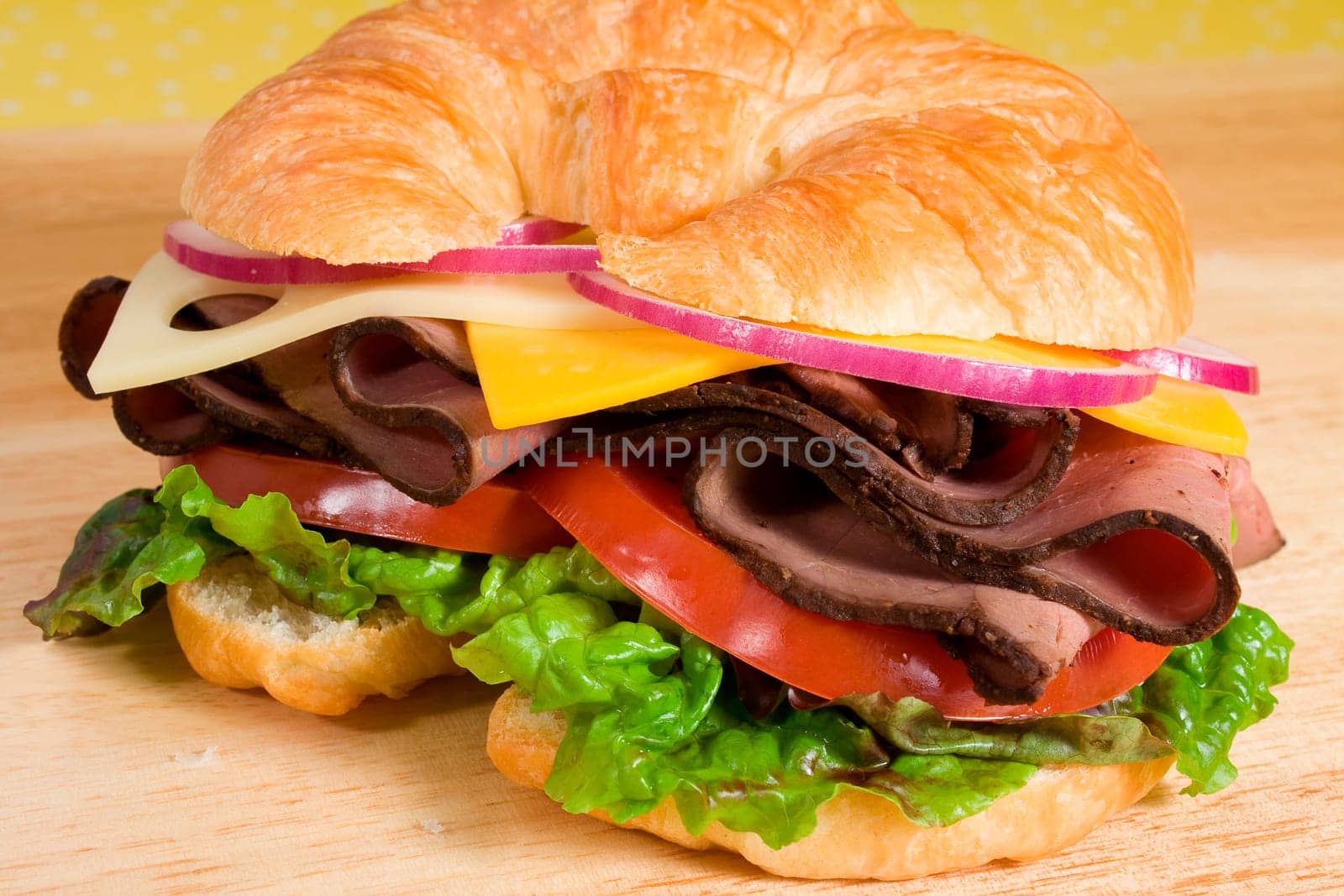 Roast beef sandwich on a croissant with cheddar and swiss cheeses, tomatoes, lettuce, and onion.