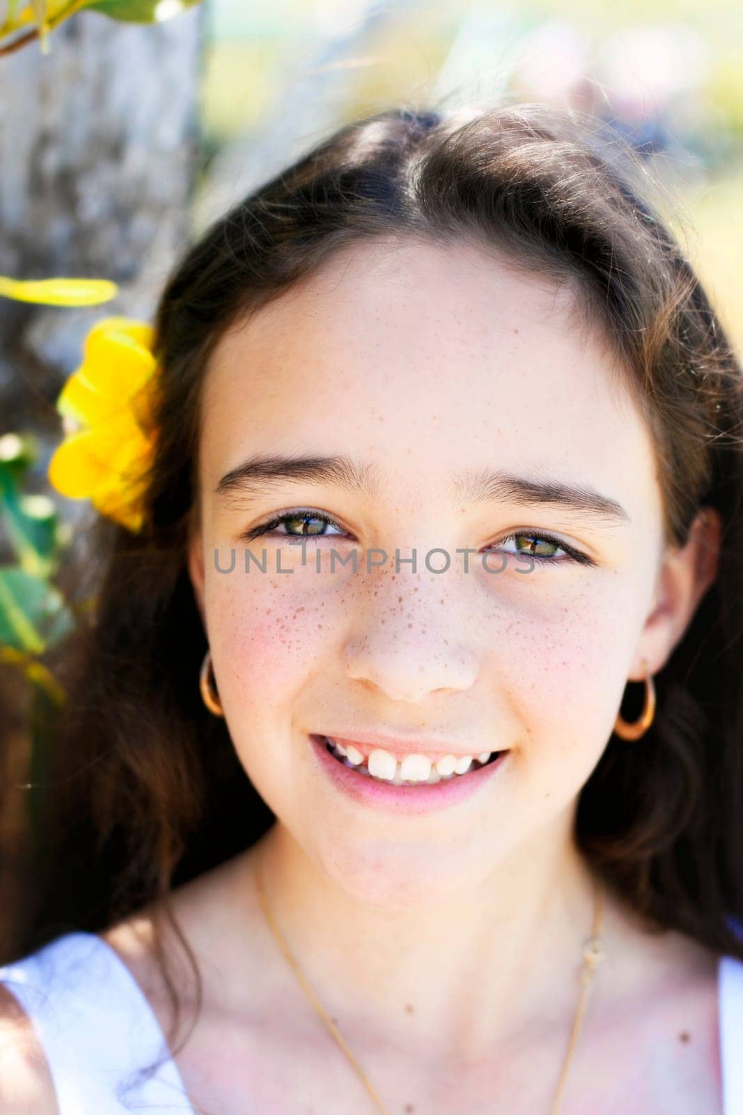A close-up portrait of a pretty, smiling, dark haired young girl outdoors.