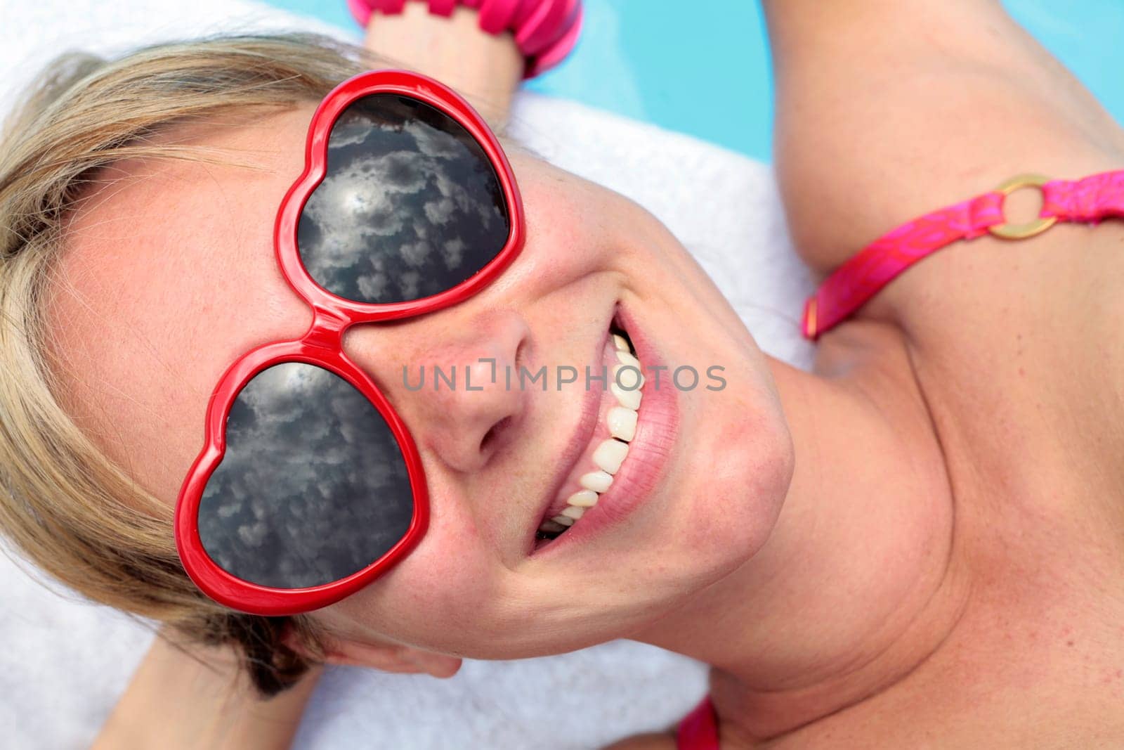 Woman in heart-shaped sunglasses besides a bright blue swimming pool