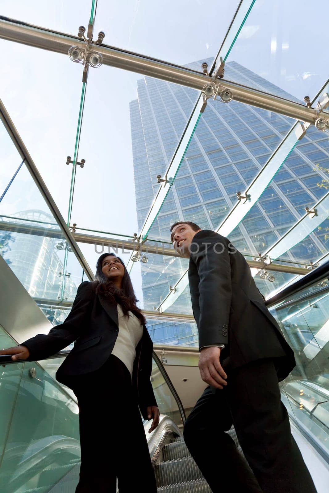 A young make and female exuctive ride an escalator together in a modern hi-tech city setting
