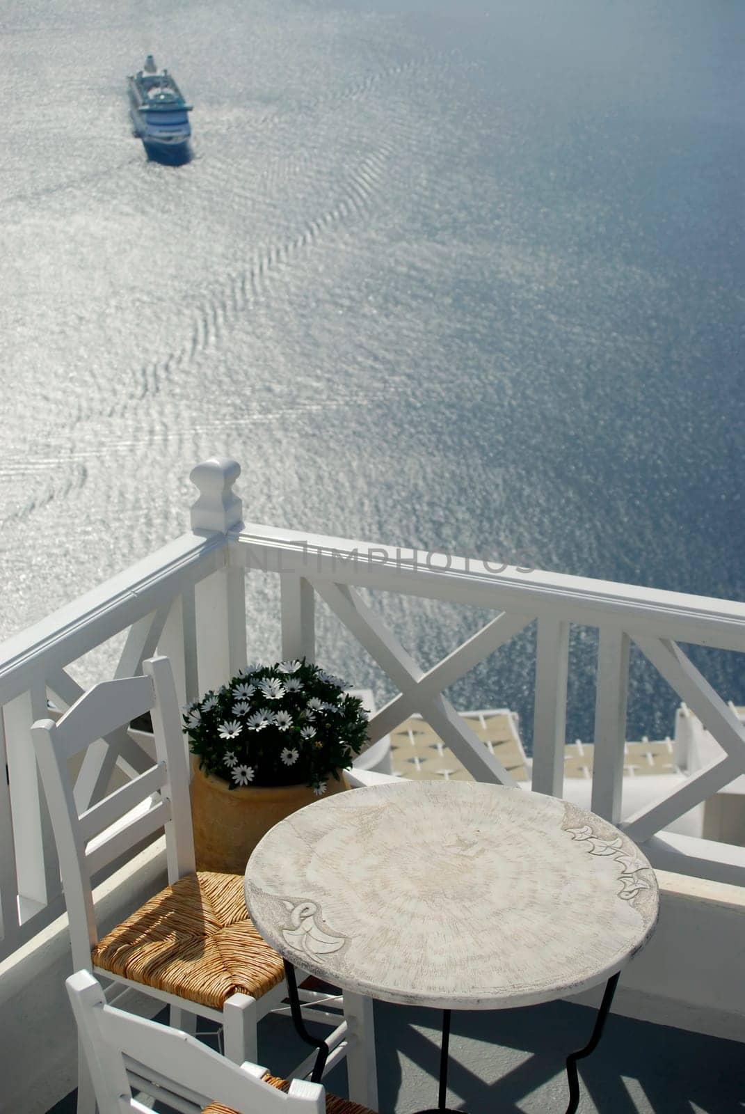 View across a balcony with table and chairs, looking down over the caldera in Santorini, where a cruise ship has arrived