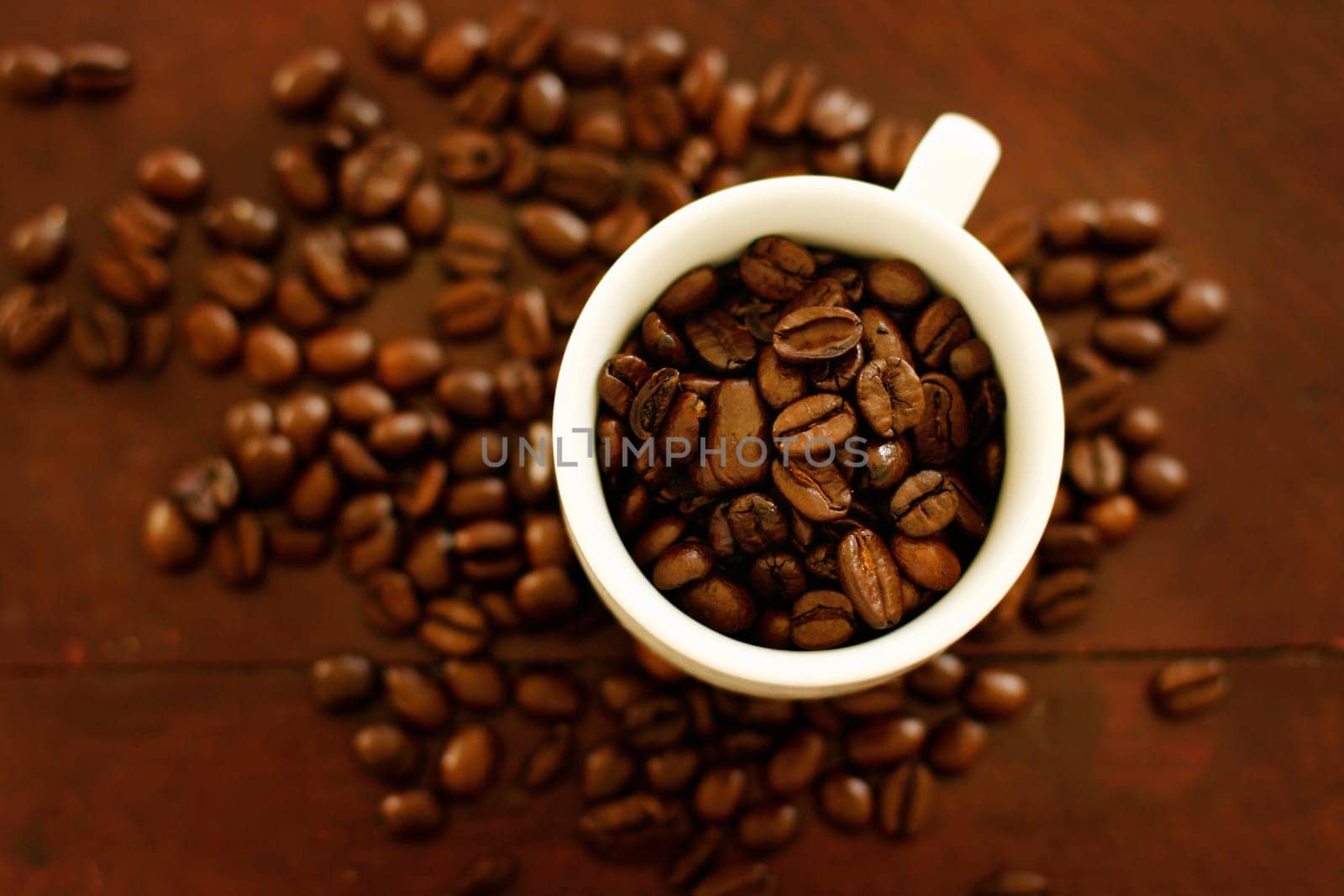 Small white cup filled and surrounded by coffee beans.