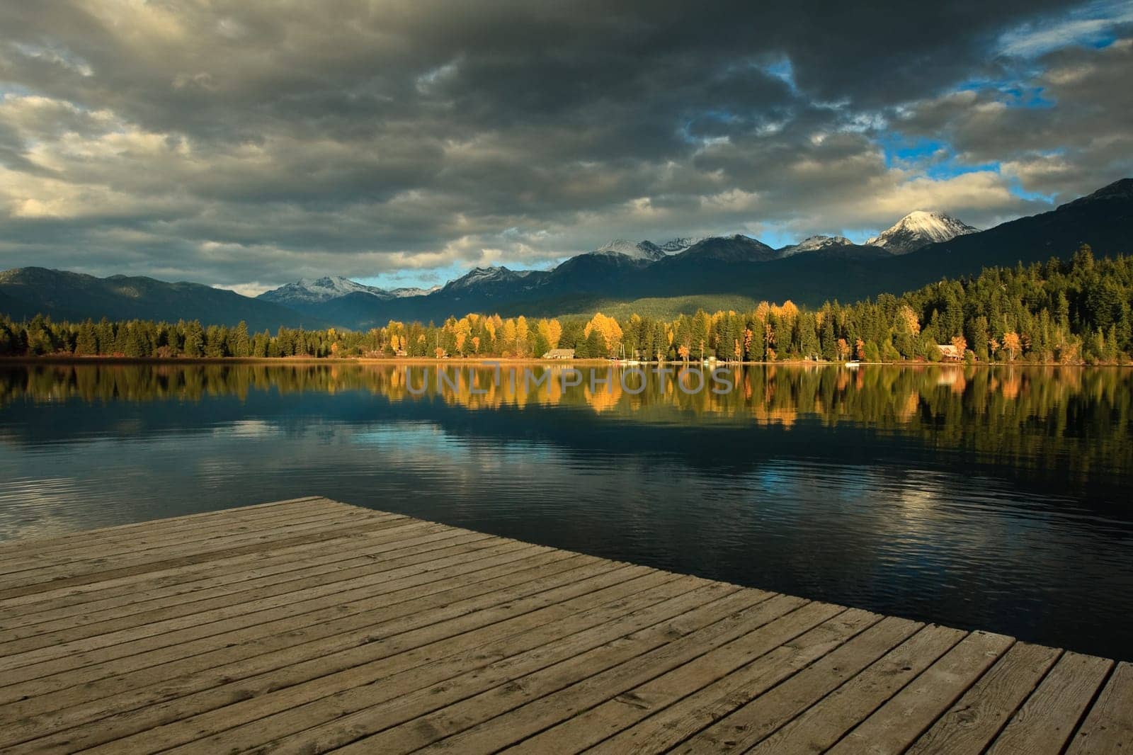 A cloudy autumn scene, is reflecting on the lake surface at the end of the quay in Whisler, British Columbia