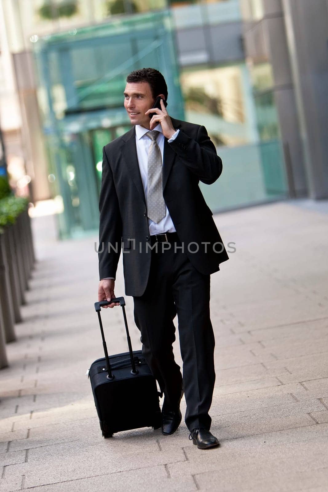 Successful bussinessman travelling with his suitcase and talking on his cell phone. Shot on location in a city or airport setting.