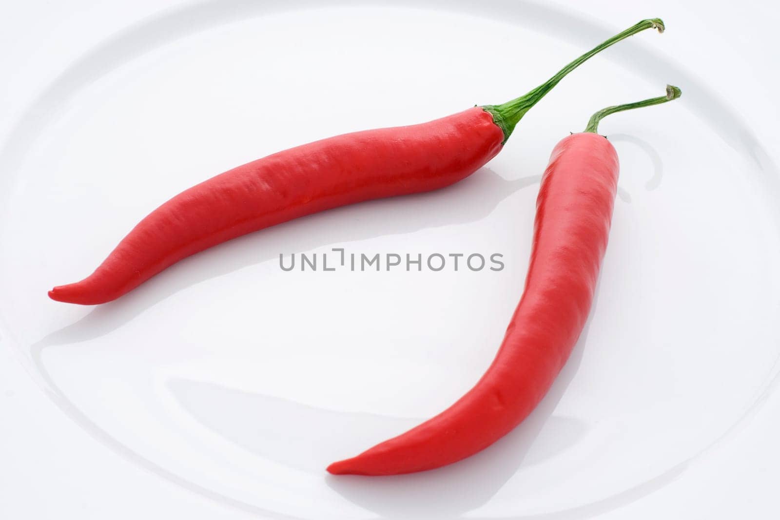 Two red peppers resting on a white plate.