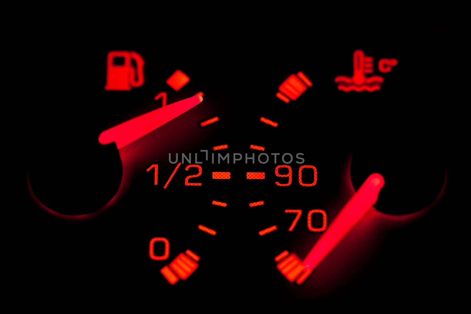 Car dashboard gauges illuminated over a black background. Shallow depth of field