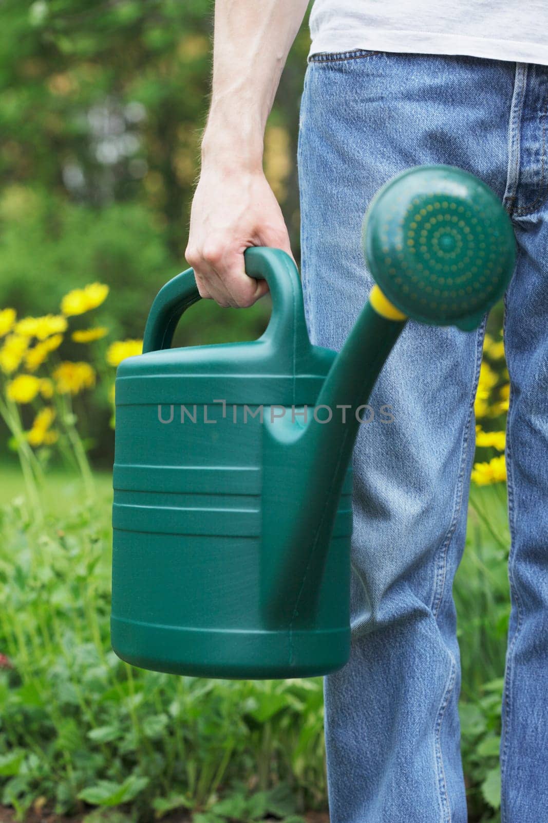 A Man holding a green plastic watering can in his hand. Short depth of field, sharpness is in the hand.