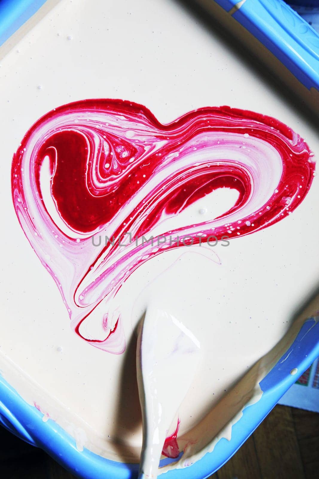 White oil paint in a blue basin with the red paint stirred as heart