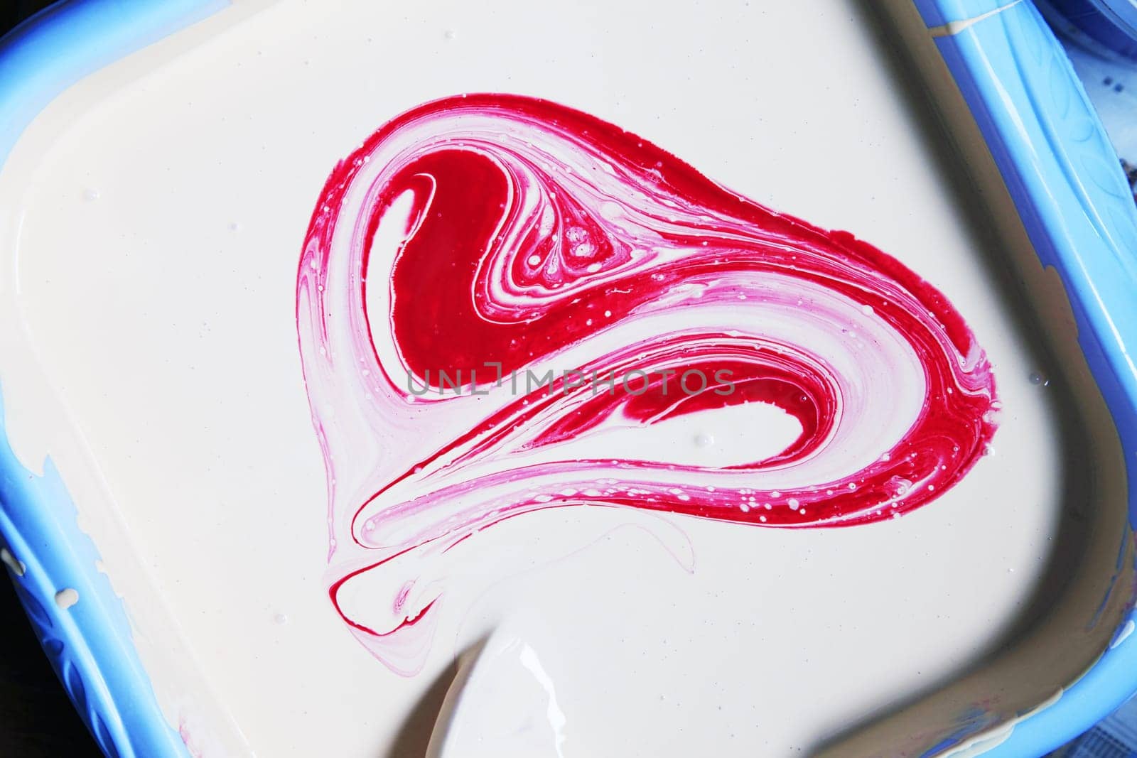 White oil paint in a blue basin with the red paint stirred as heart