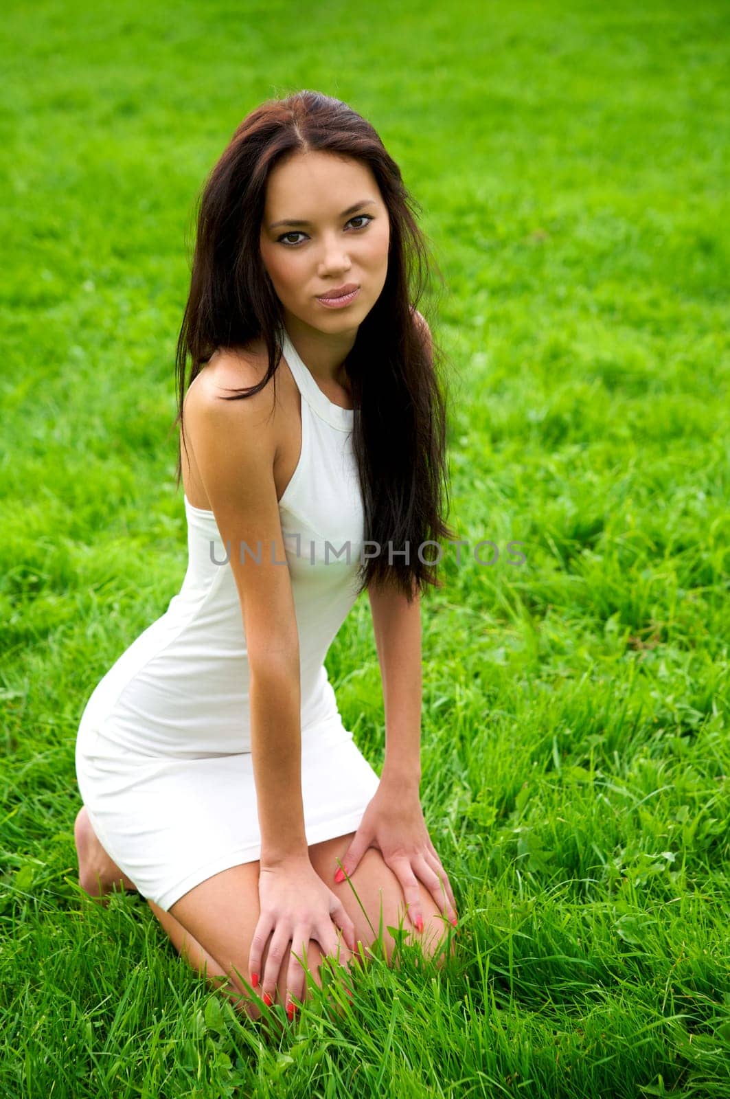 Beautiful young woman in white dress sitting on the green grass