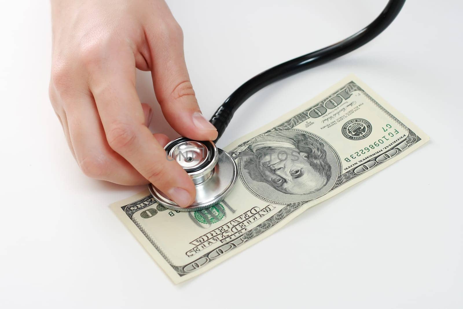Doctor holding stethoscope in her fingers against one hundred u.s. banknote at the white table