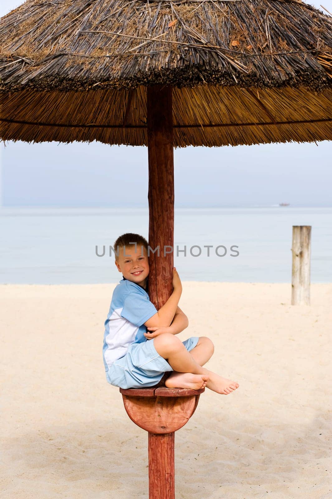 Little boy under a beach umbrella near the sea summer dress