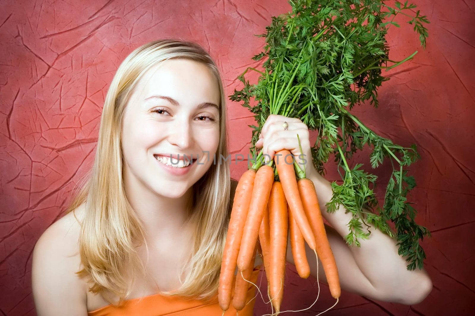 Smiling young woman with fresh carrots. Red background.