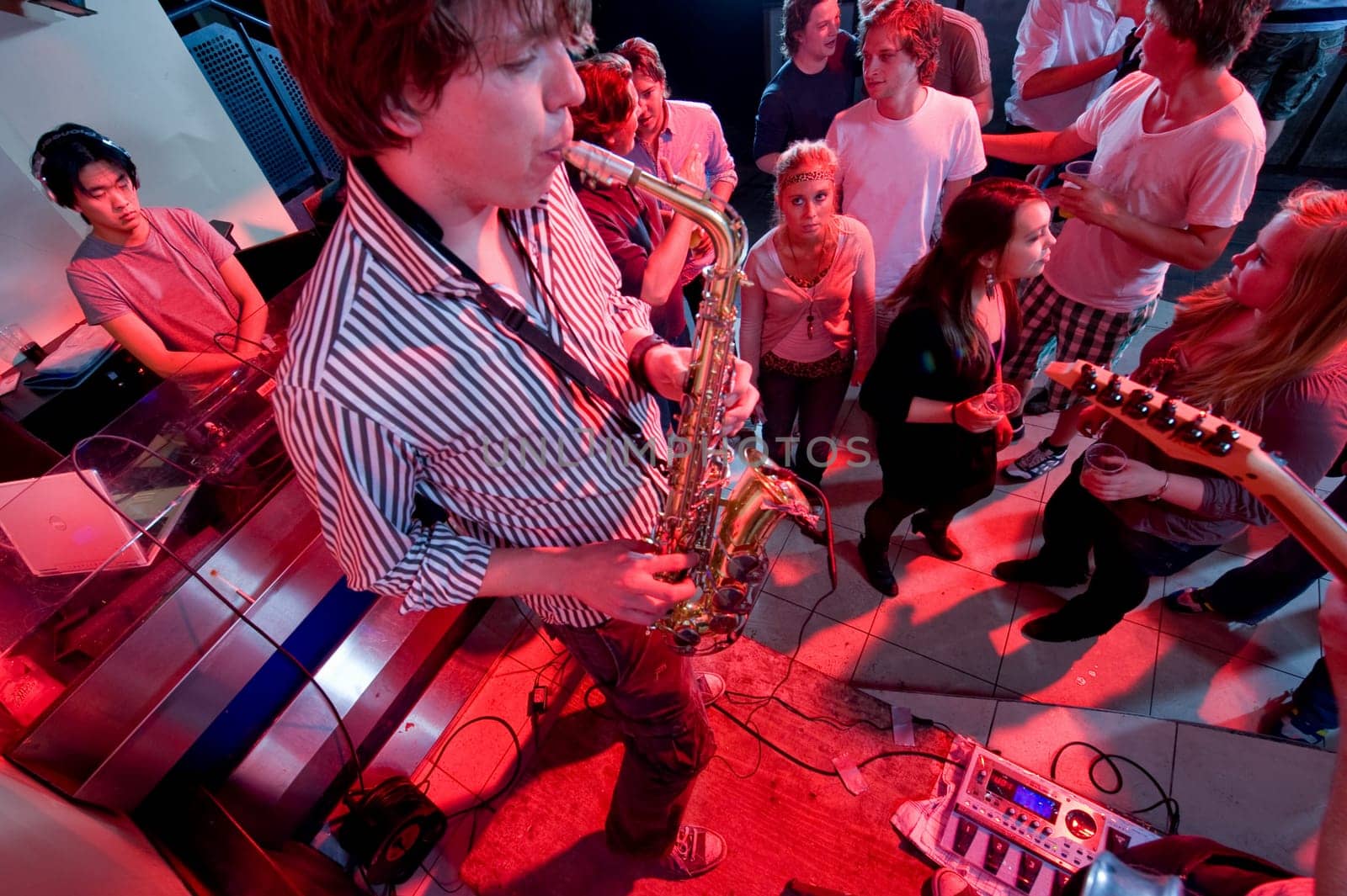 A performance of a saxophonist and guitarist in a nightclub with DJ.