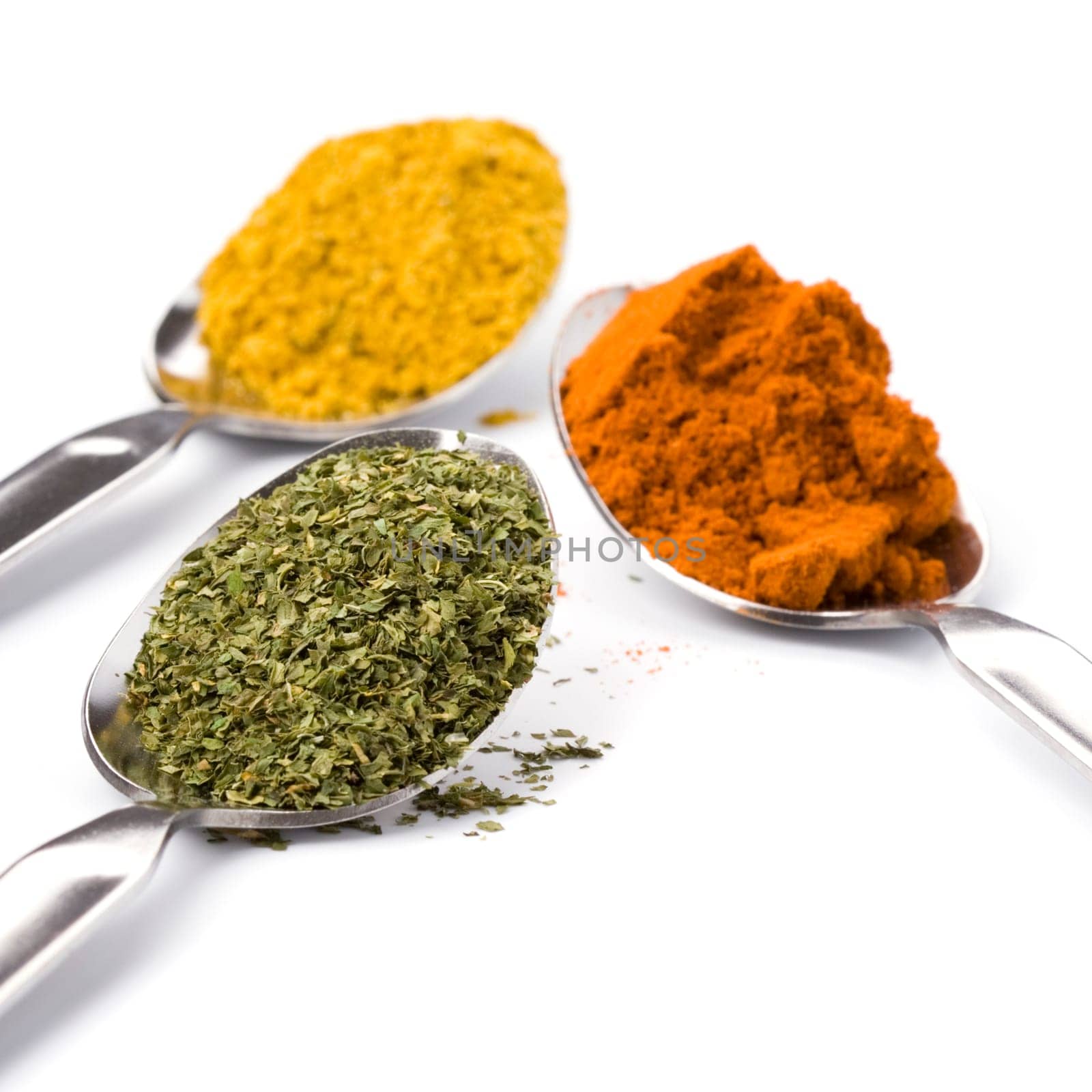metal spoons with various ground spices on white background