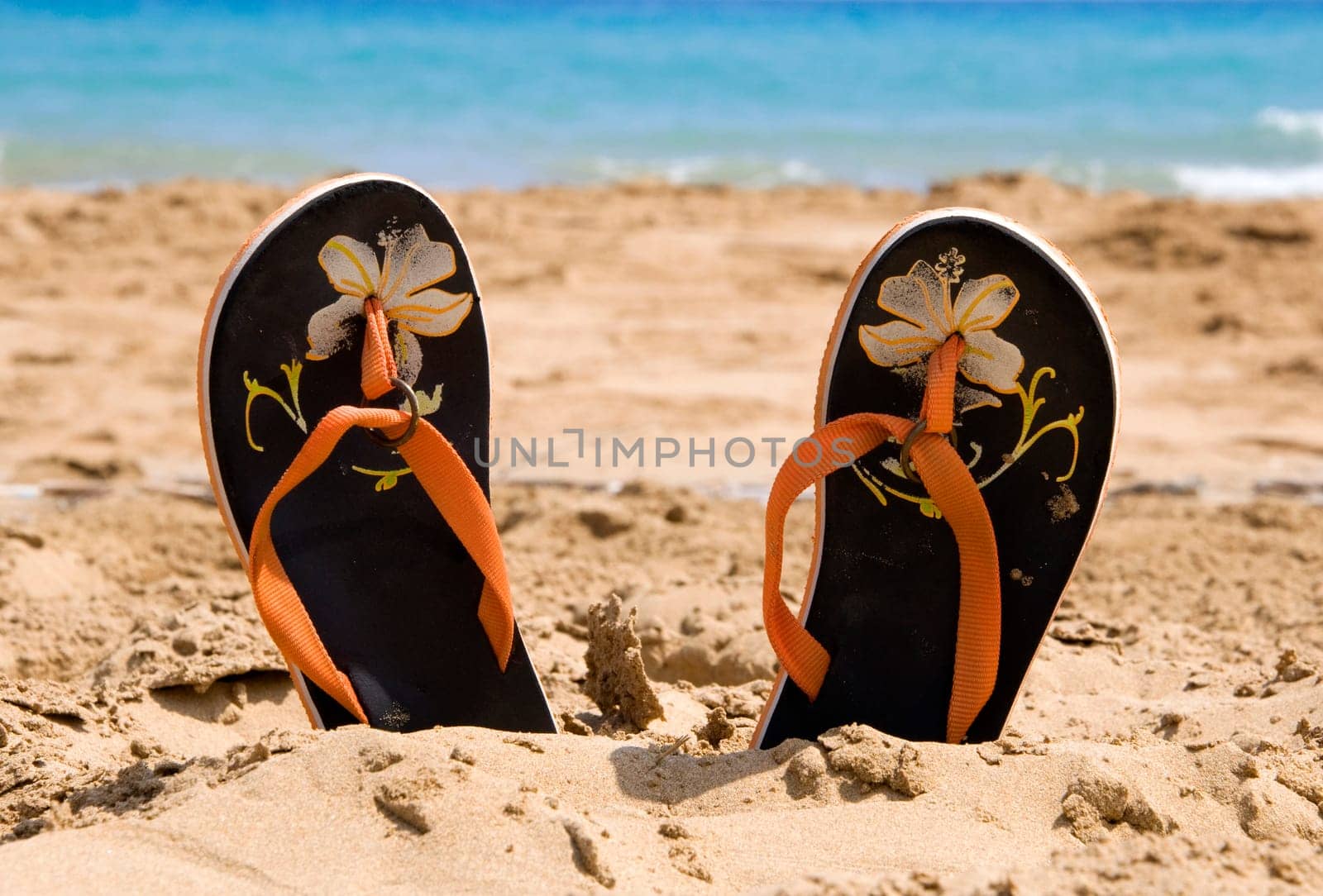 Pair of sandles on a beach with the sea in the background