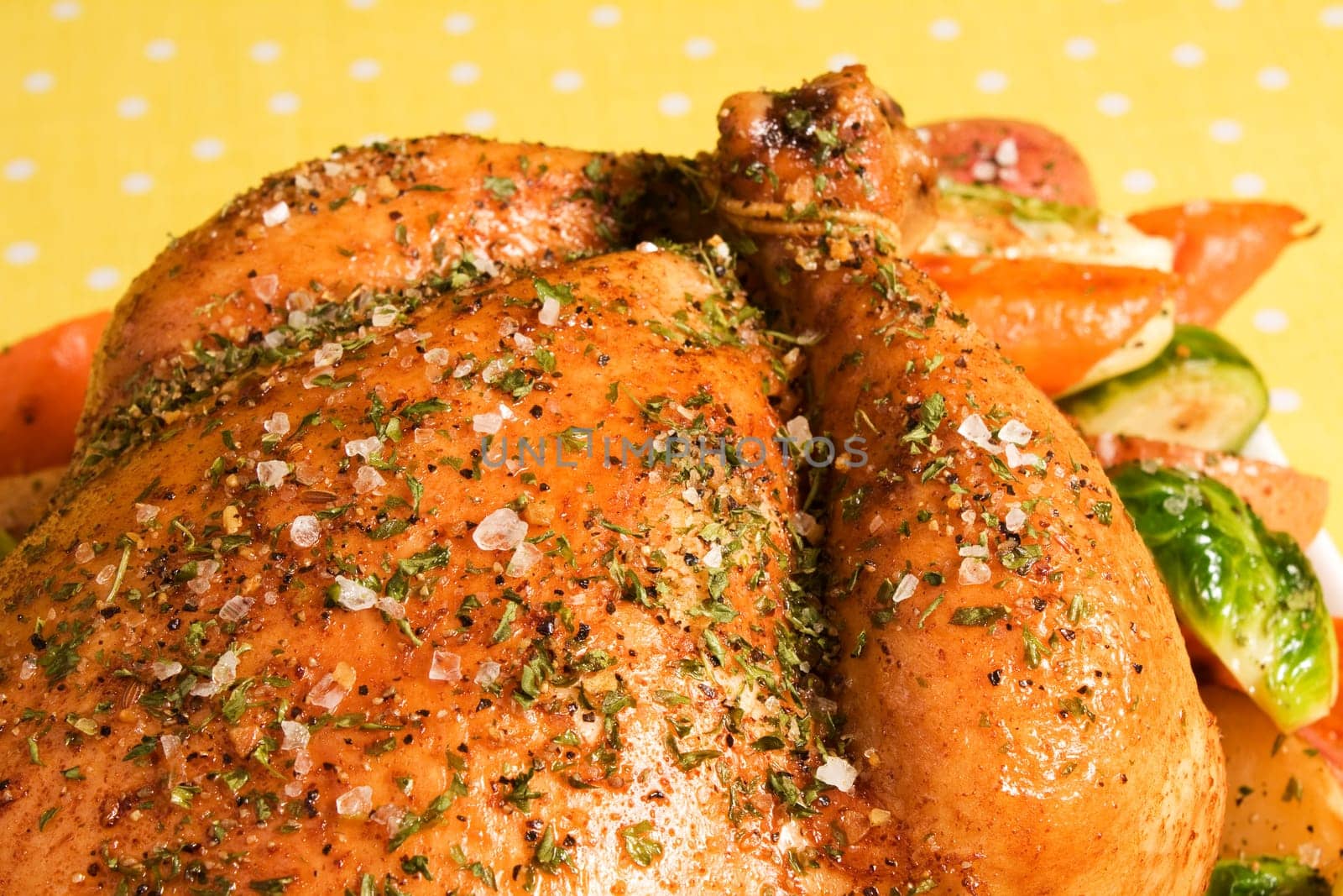Roasted chicken seasoned with herbs and garnished with potatoes, carrots, and brussels sprouts.