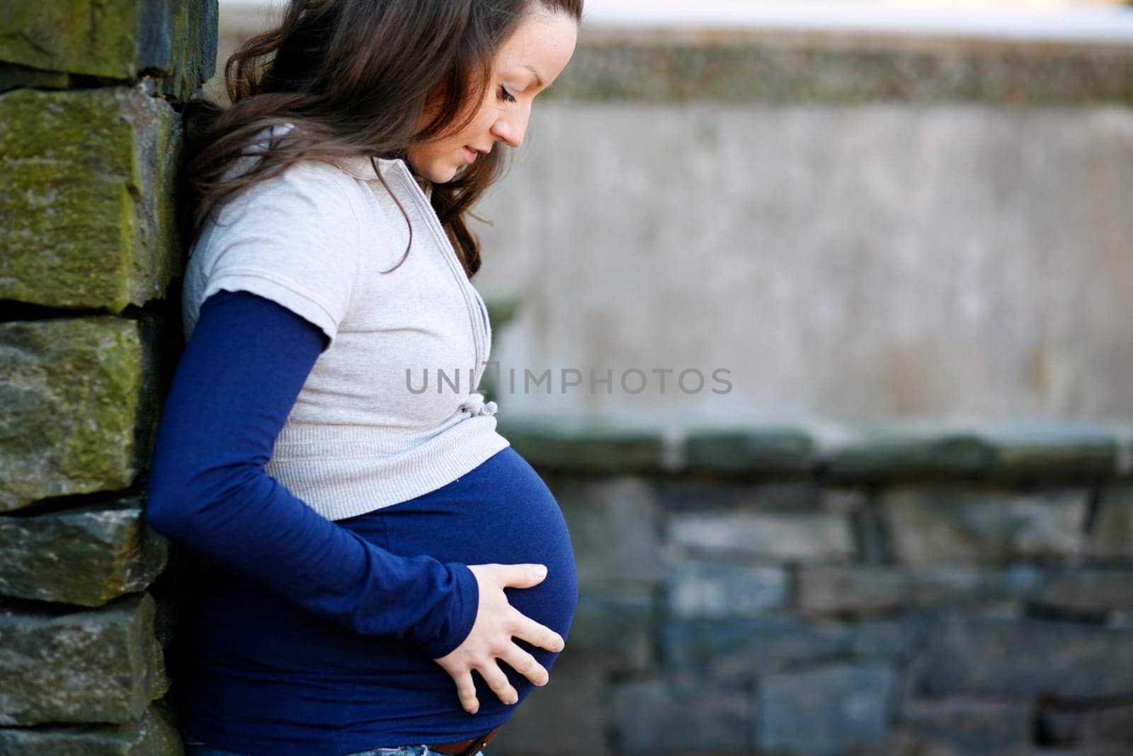 A young pregnant woman holding her time while outdoors.