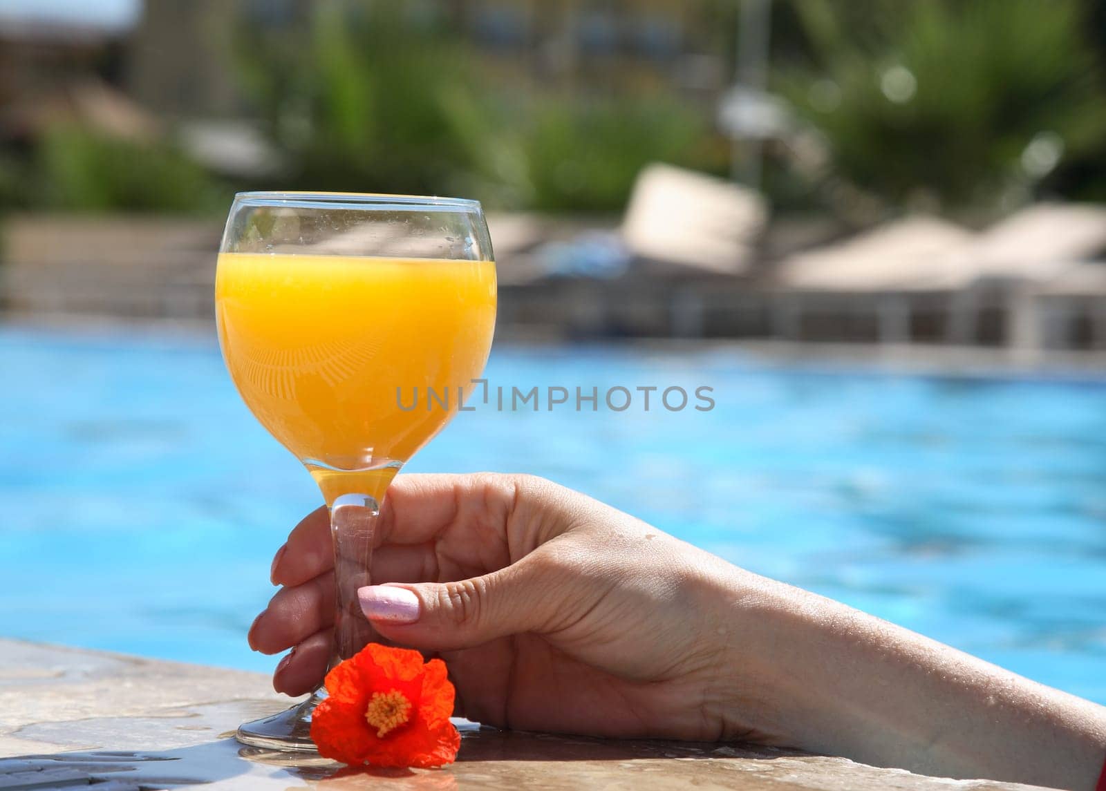 female hand holds a glass with juice in pool