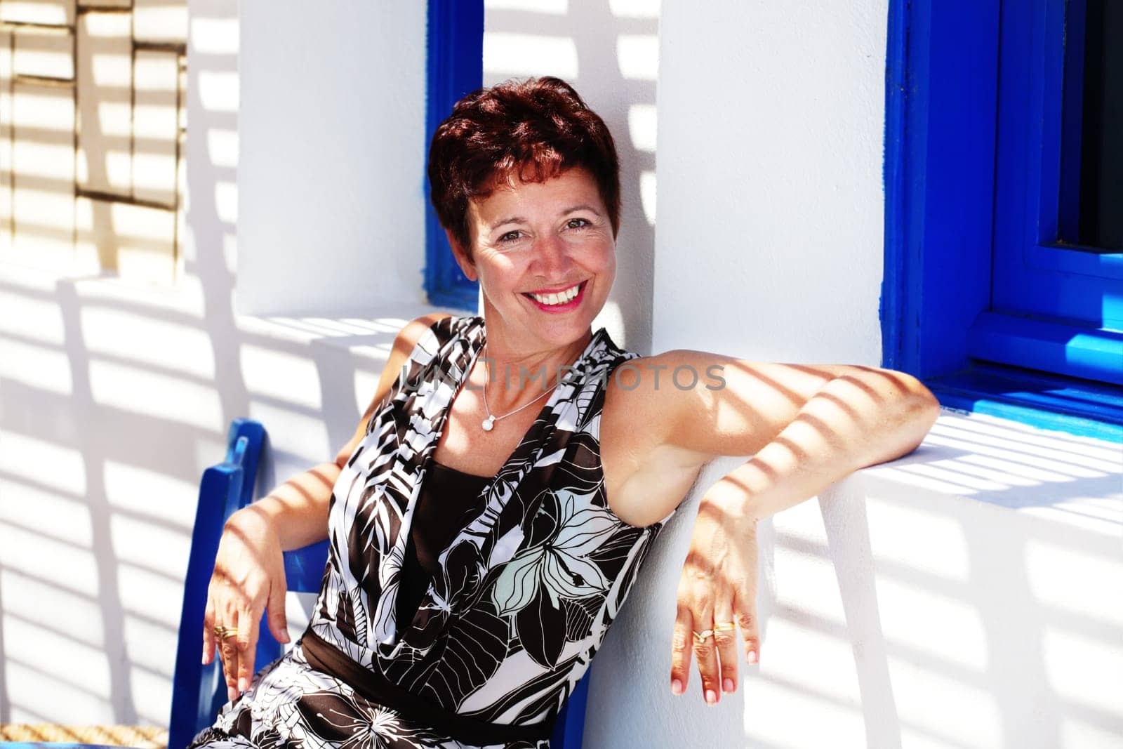 beautiful mature woman relaxing in the shadow of a pergola and smiling at the camera