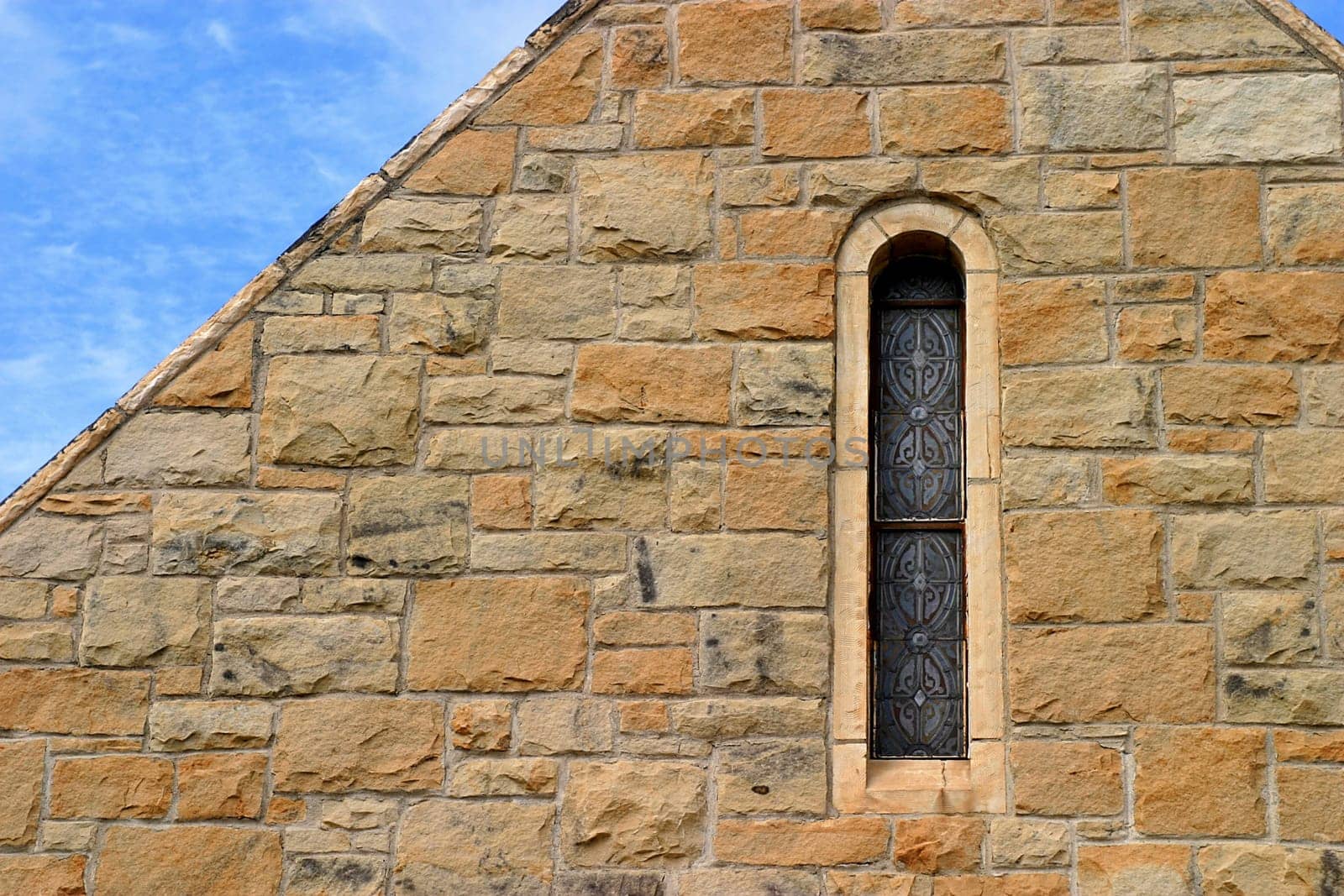 Small church window in stone wal with sky.