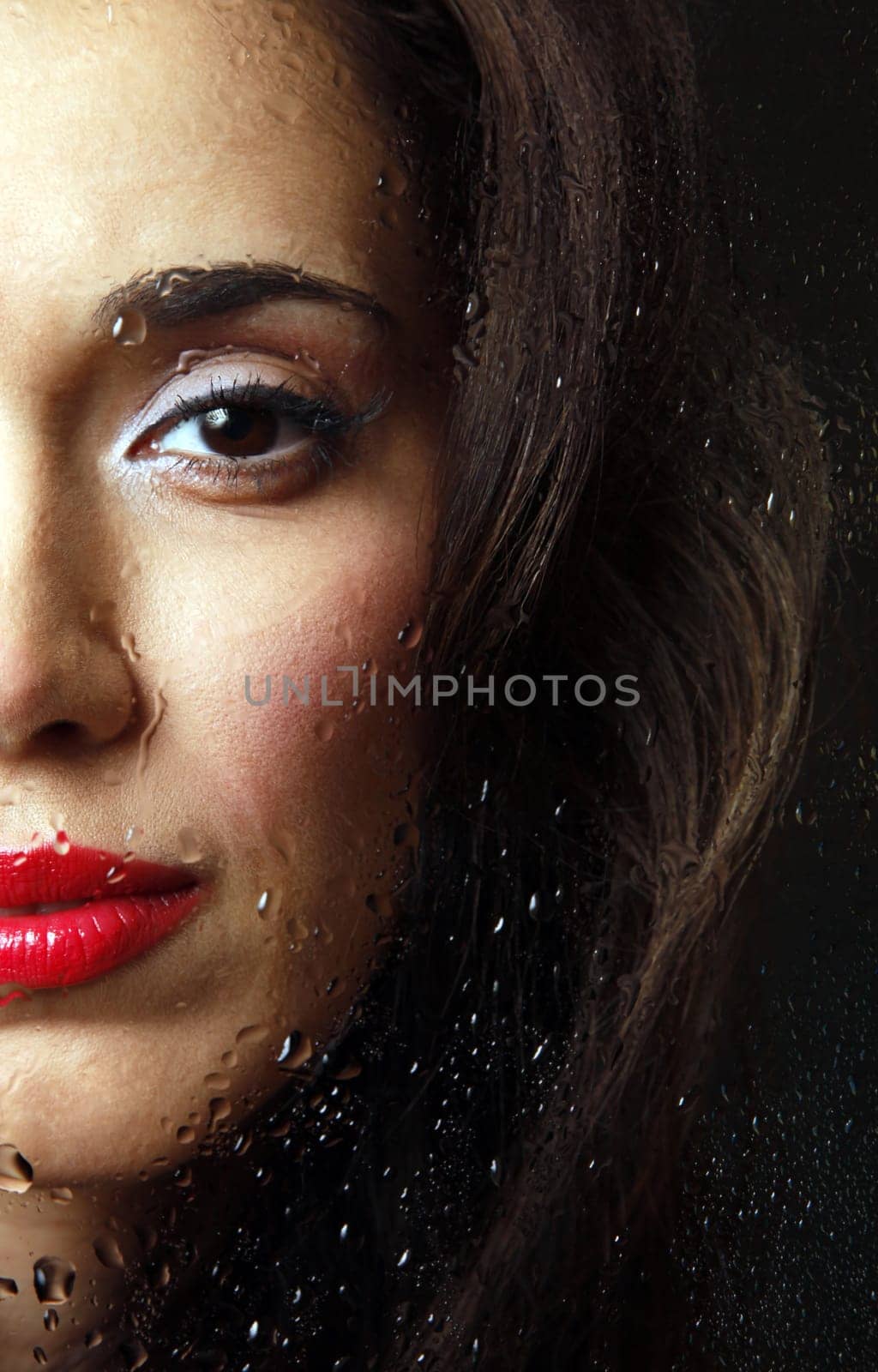 The beautiful girl behind wet glass