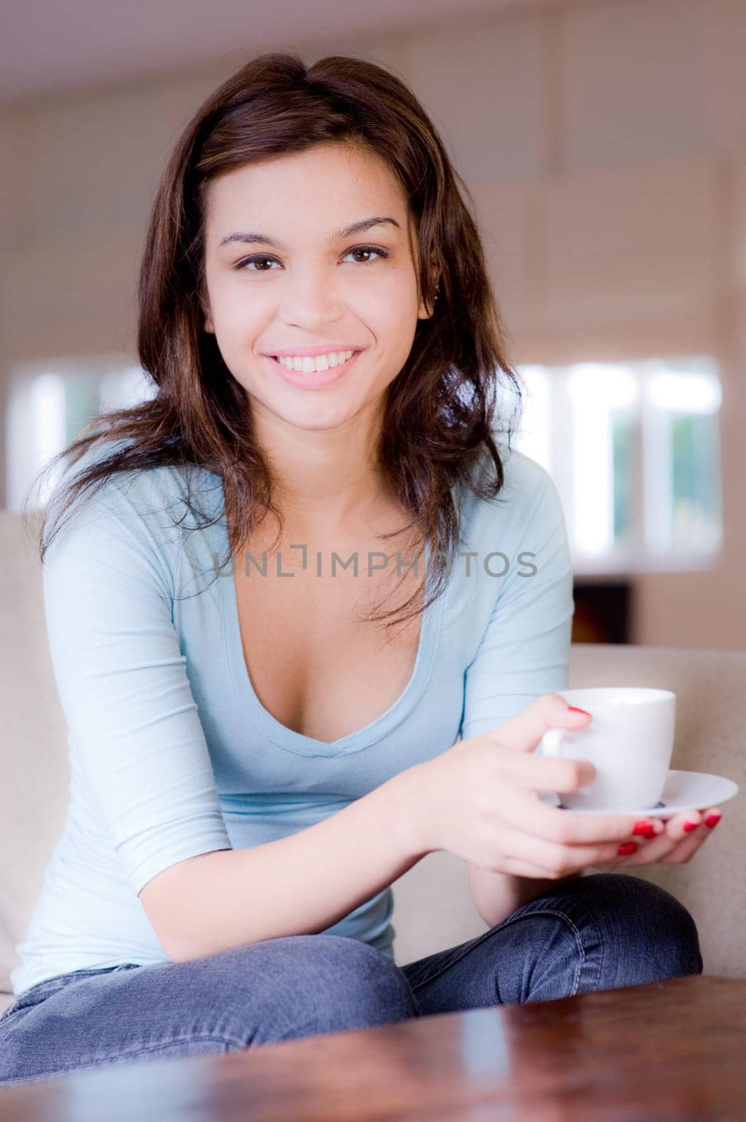 A young woman at home on sofa holding cup and saucer