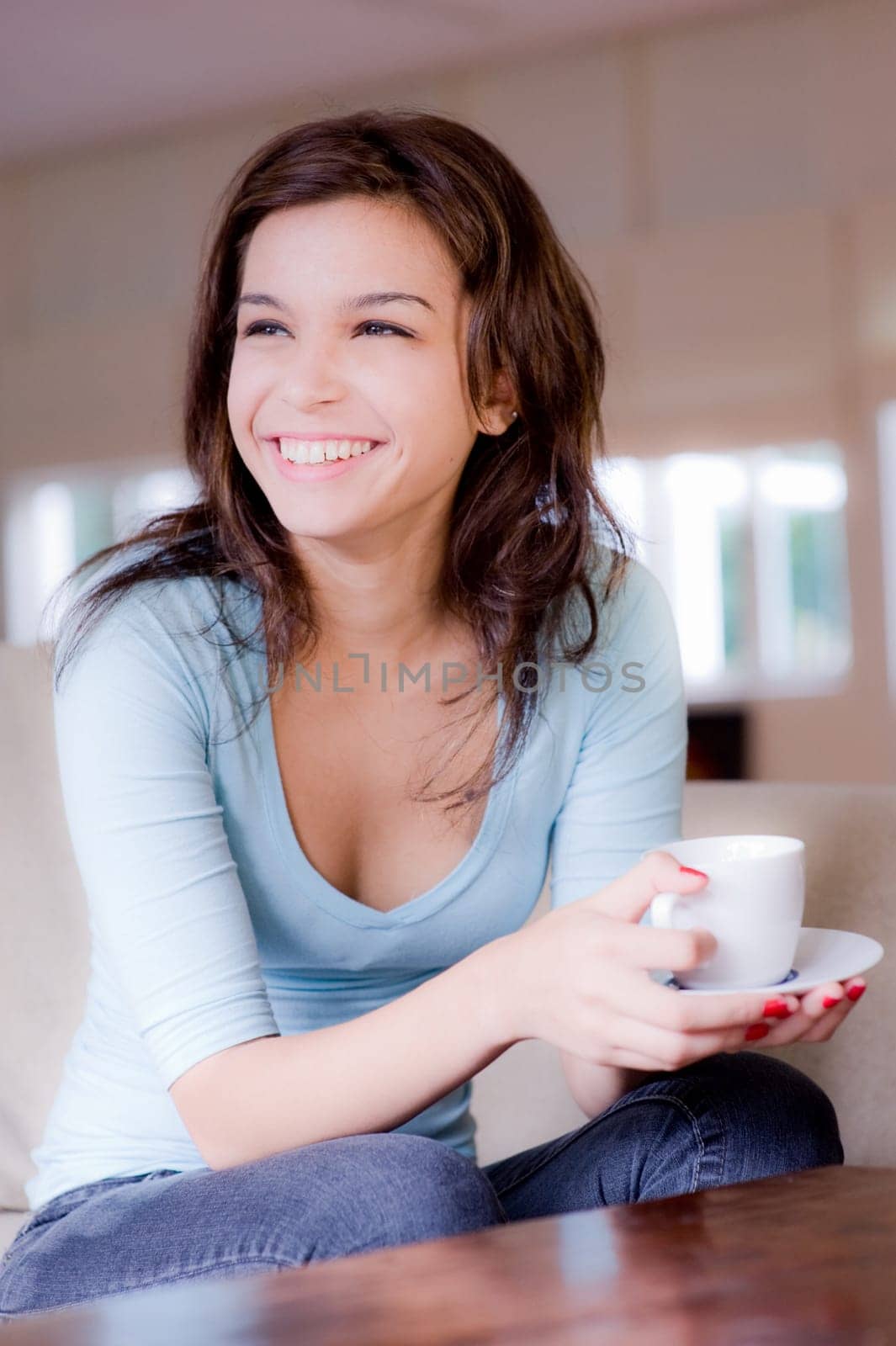 A young woman at home on sofa holding cup and saucer