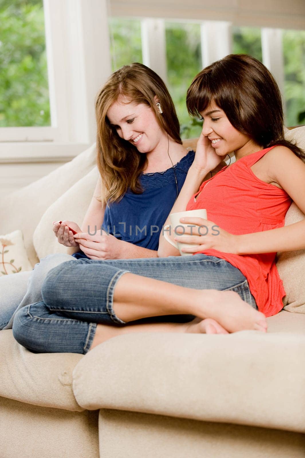 Two young woman at home on the sofa listening to music