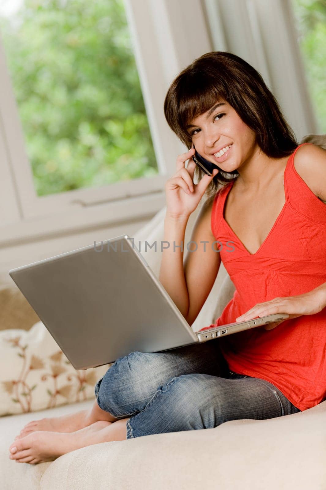 A woman sitting at home on the sofa with laptop computer and phone