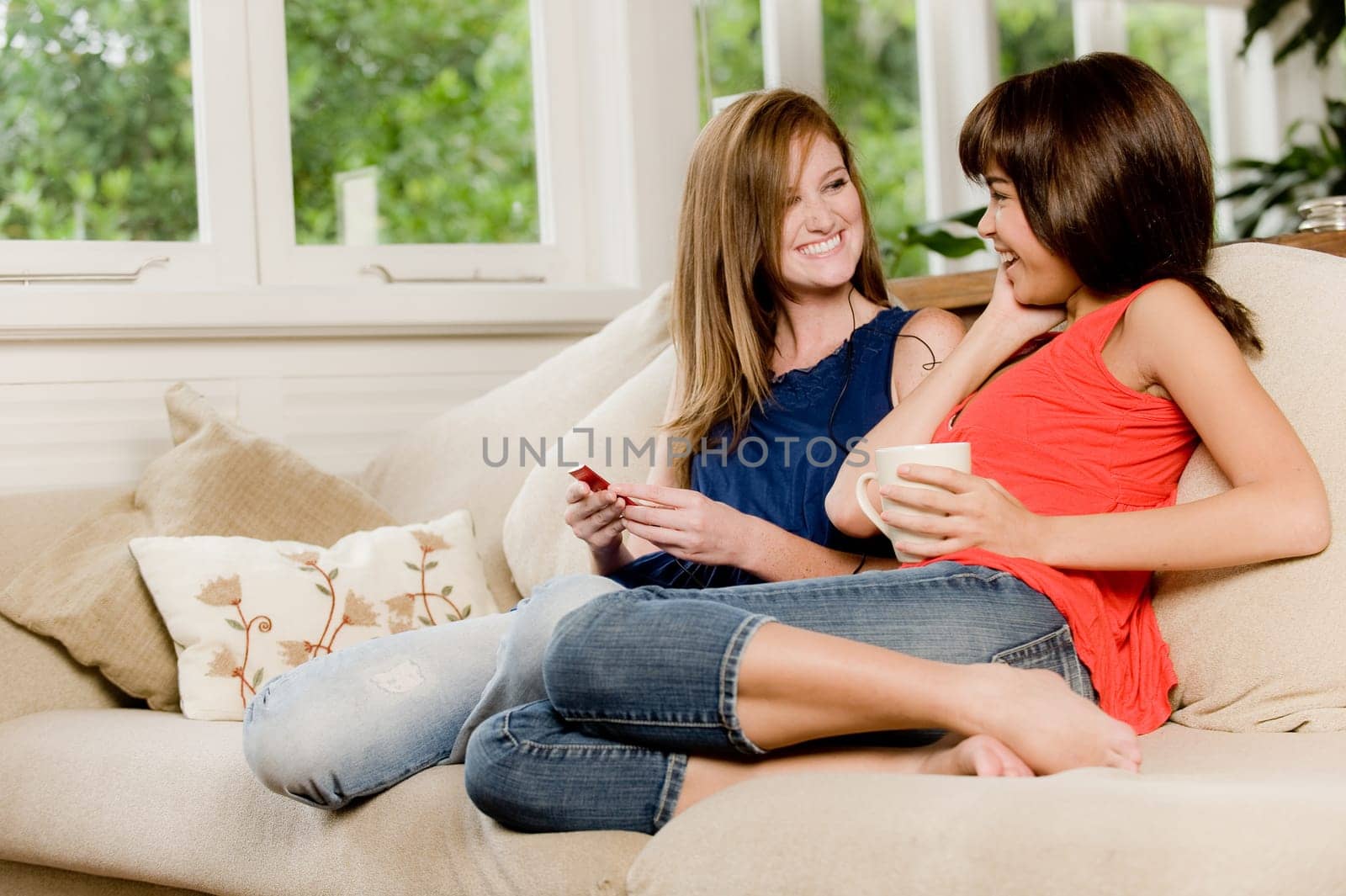 Two young woman at home on the sofa listening to music