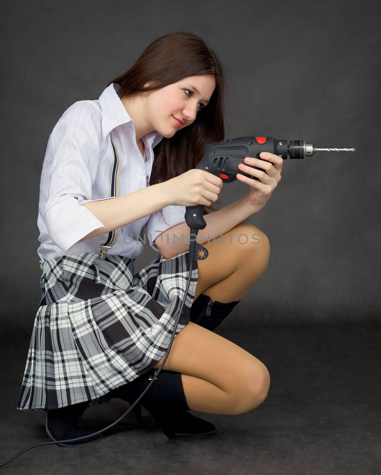 Beautiful girl in a skirt works by means of a drill