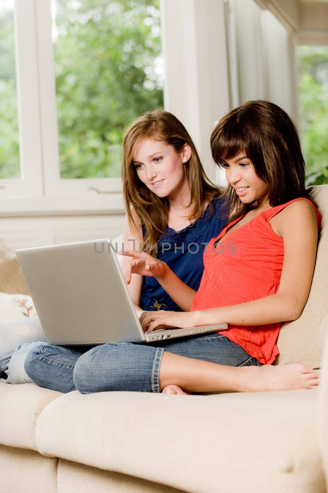 Two young woman at home on the sofa with laptop