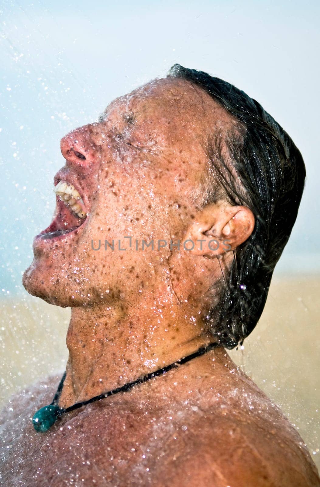 A handsome forties man is taking a wash under a powerful shower at the beach.