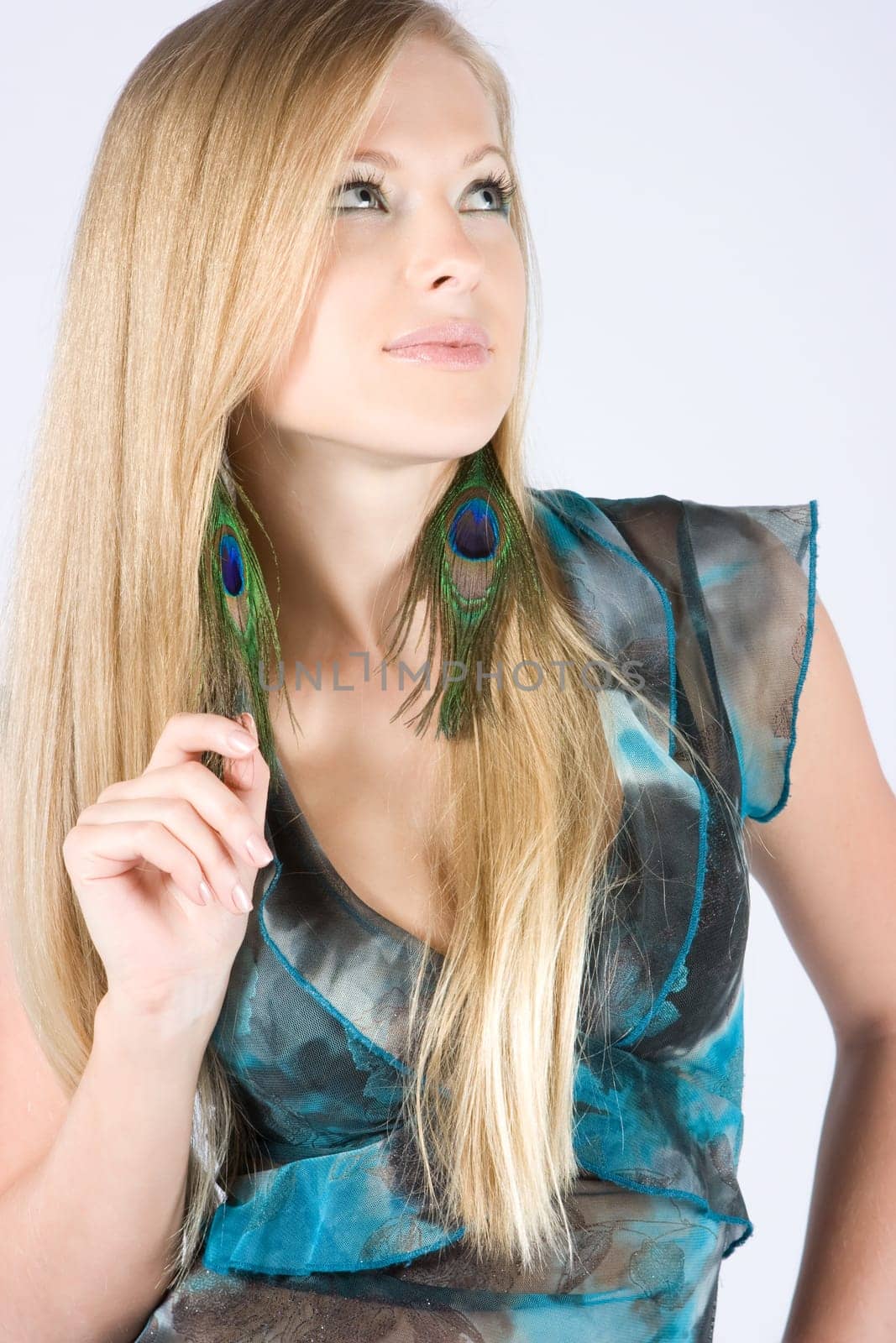 Beautiful young blond model with peacock earrings posing in studio shot