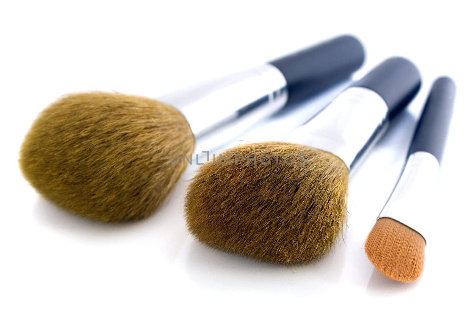 Set of three makeup brushes for face powder, concealer and eye shadow, on white background.
