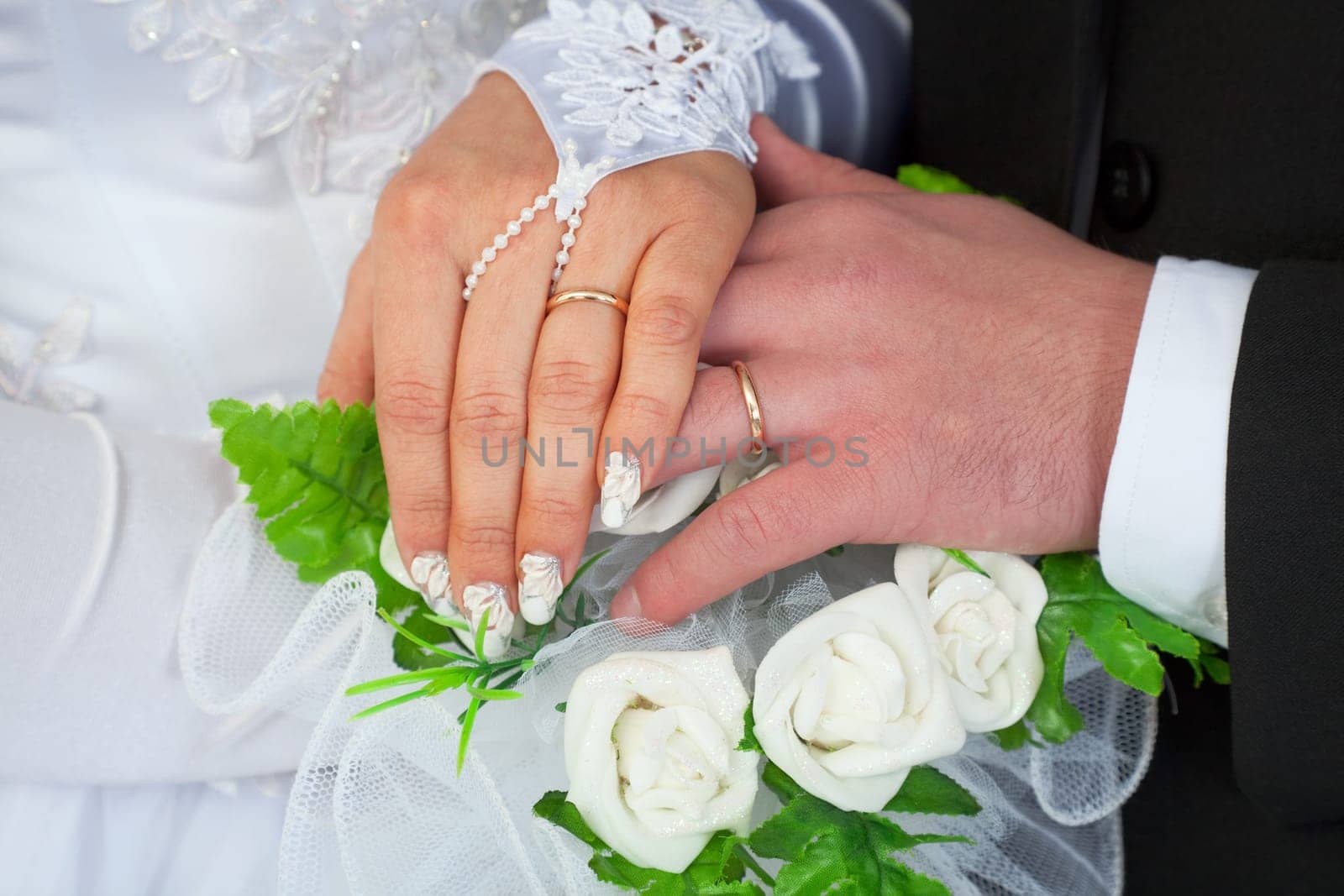 Hands of a newly-married couple with wedding rings against a bunch of flowers