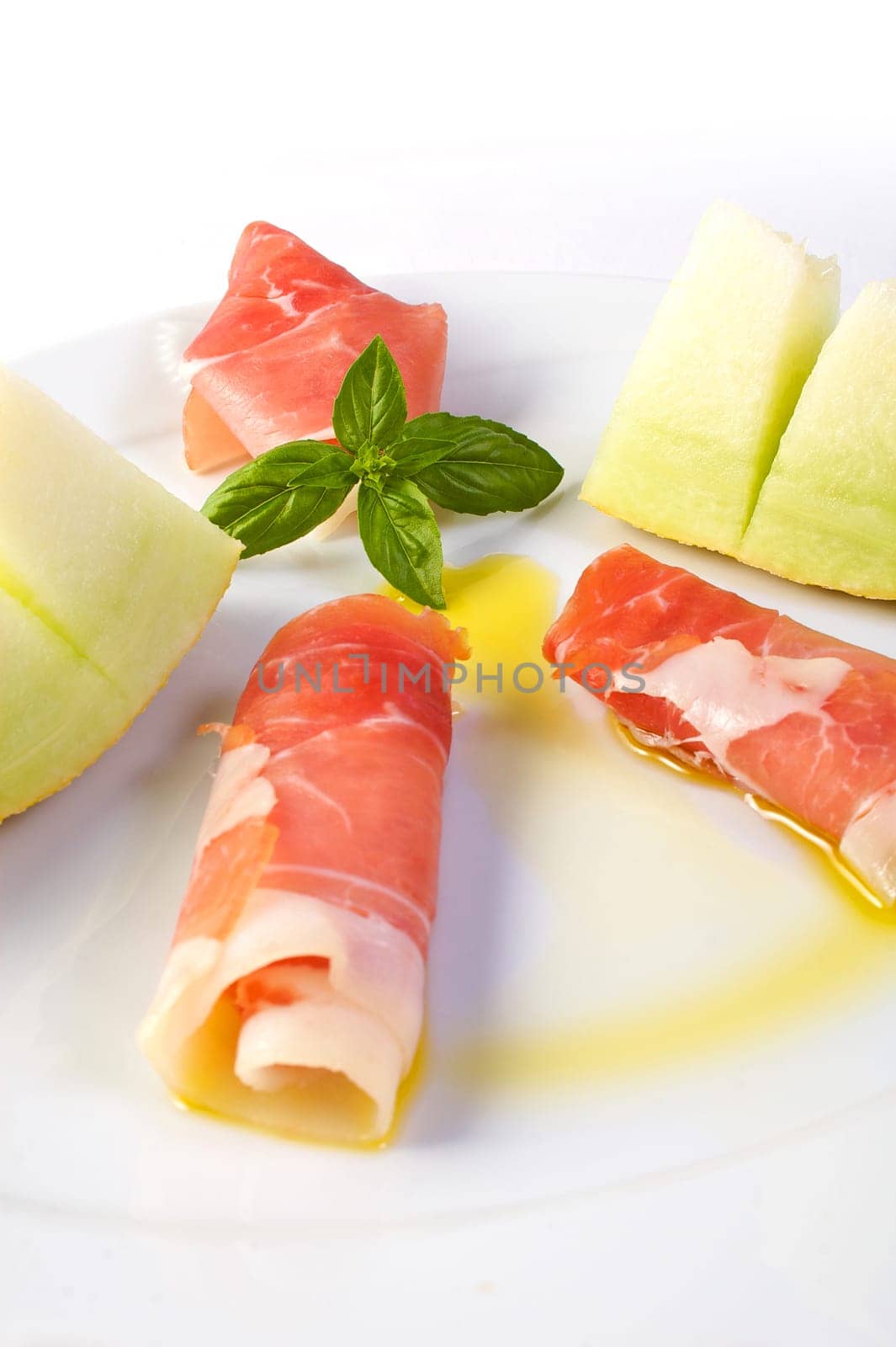 A dish with raw ham, yellow melon and olive oil garnish