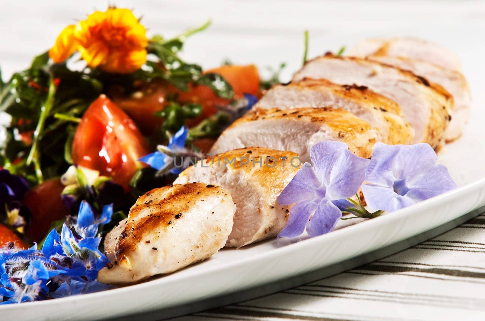 Grilled chicken breast served with salad and garnished with edible flowers