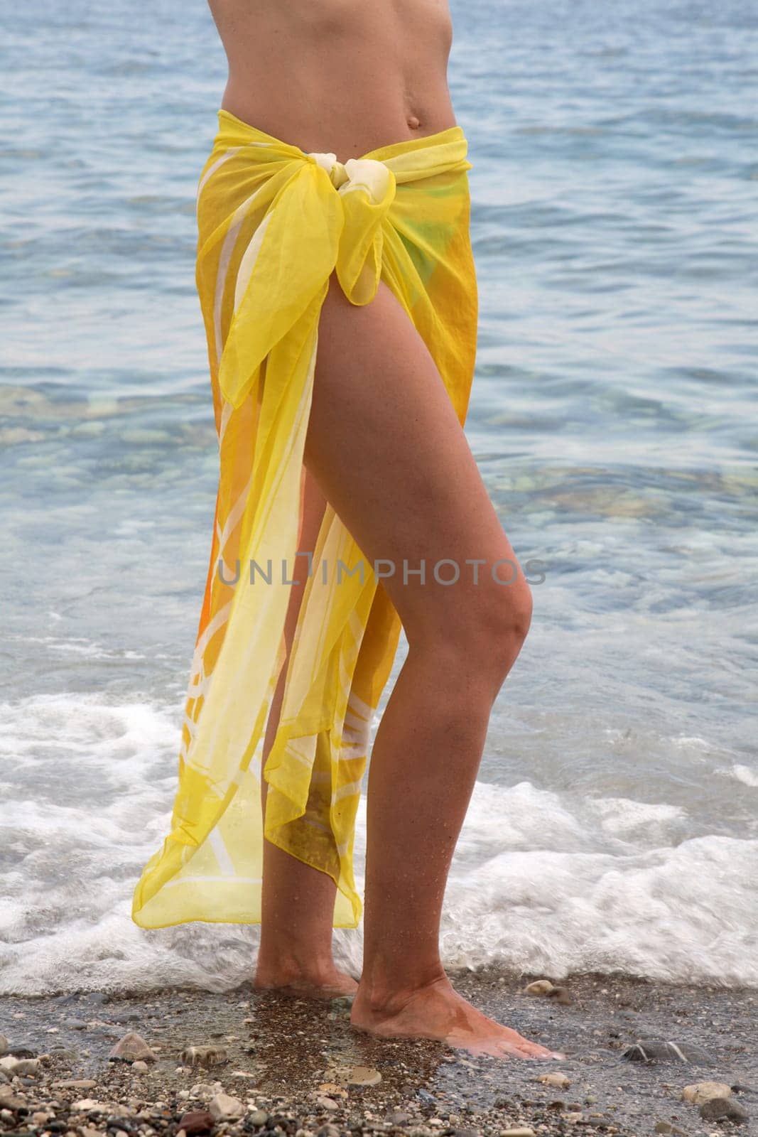 Feet of the girl in the yellow cape going on seacoast
