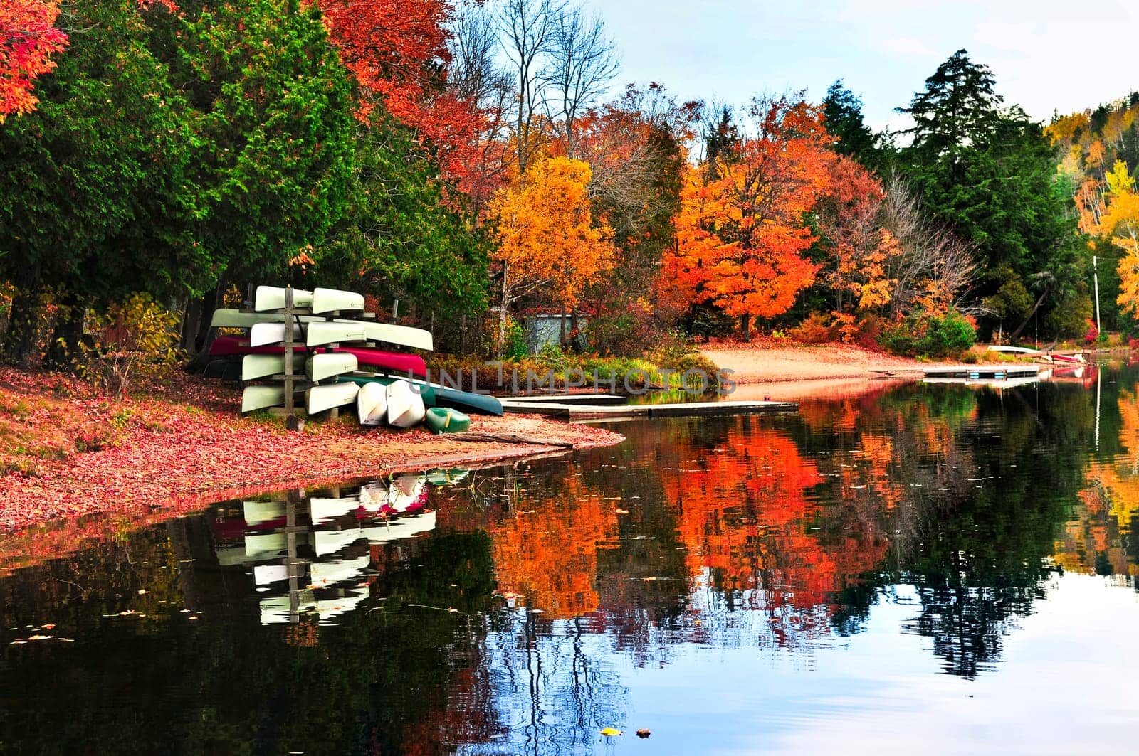 Canoes at forest of colorful autumn trees reflecting in calm lake