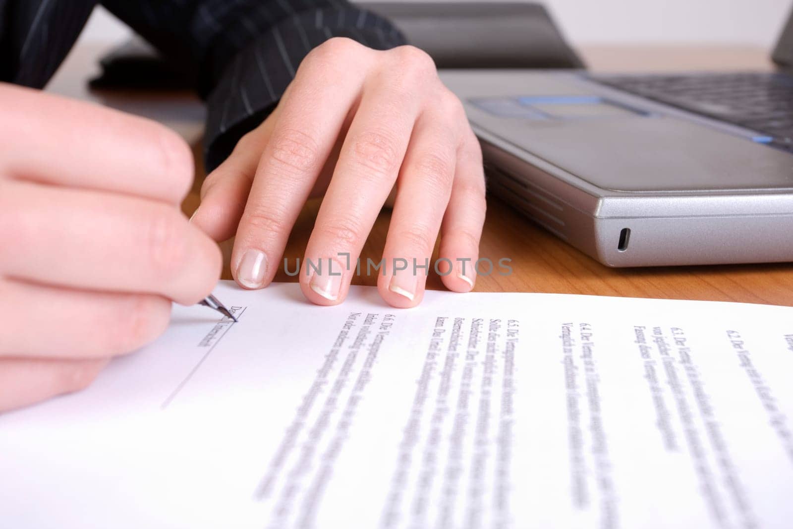 Hands signing a contract with laptop in background