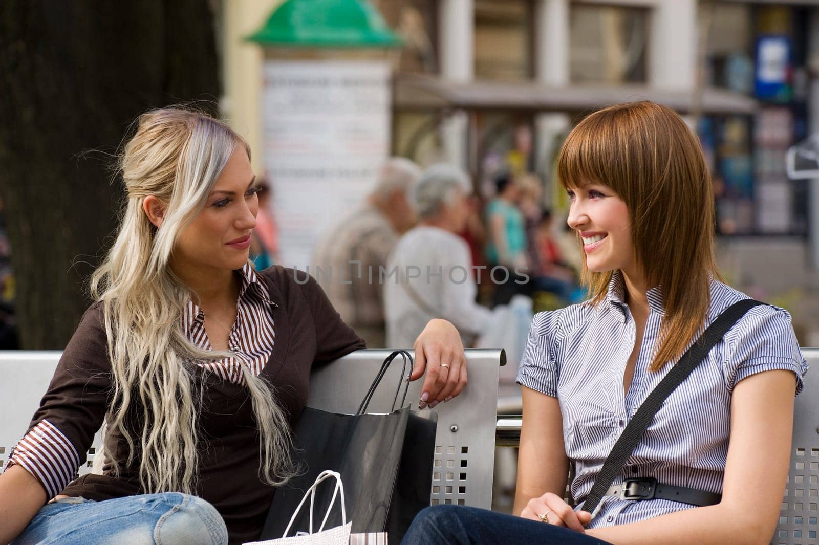 two nice girls sitting on a bench outdoor and chatting each other and smiling