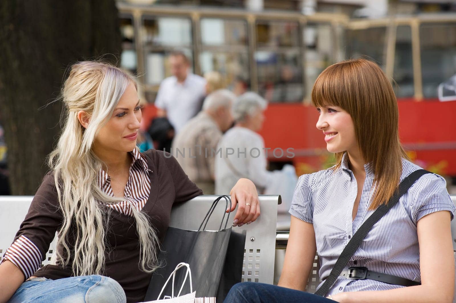two nice girls sitting on a bench and chatting each other during a shopping day