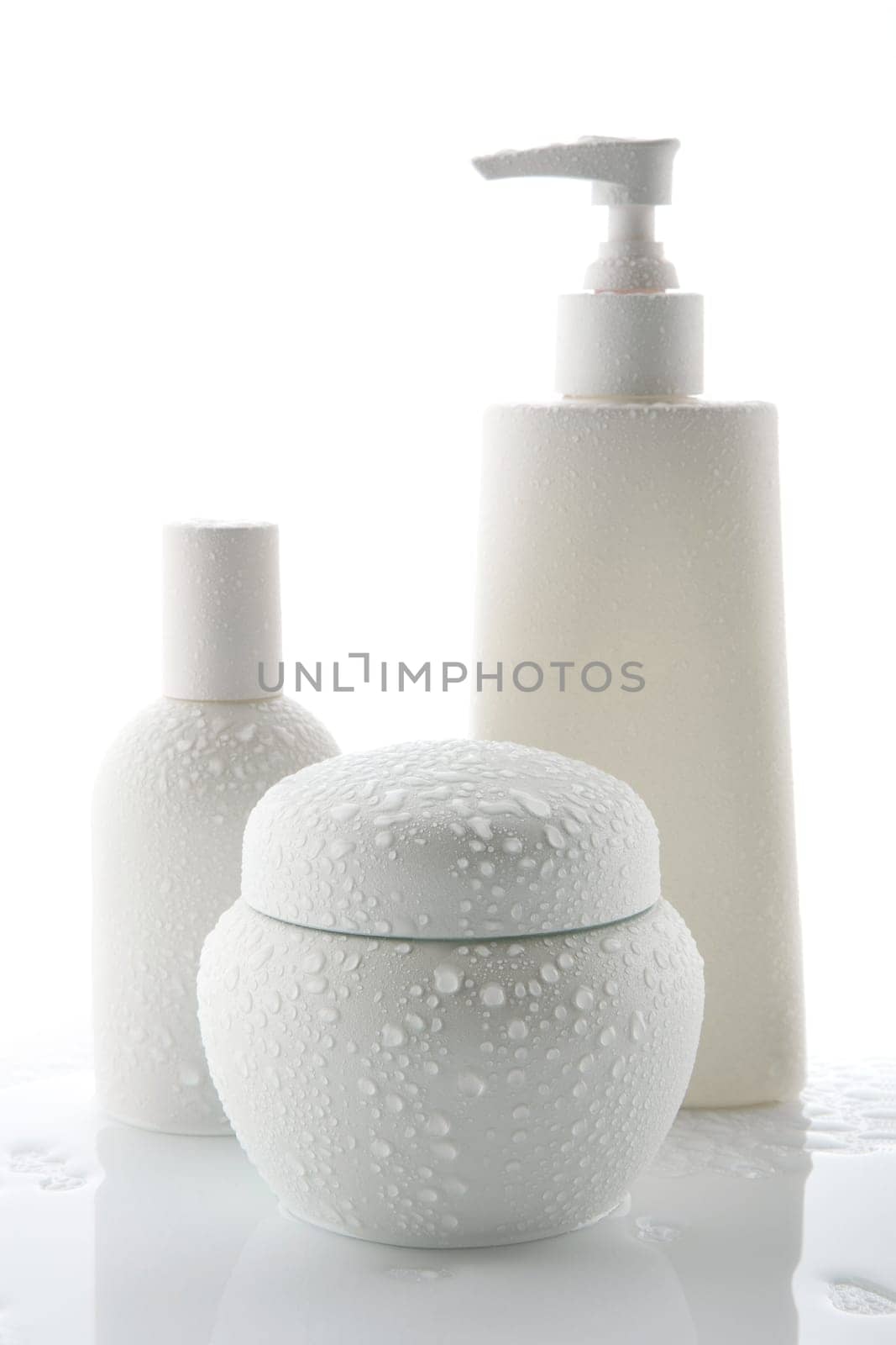 Three white cosmetic bottles with water drops, stand on a white background