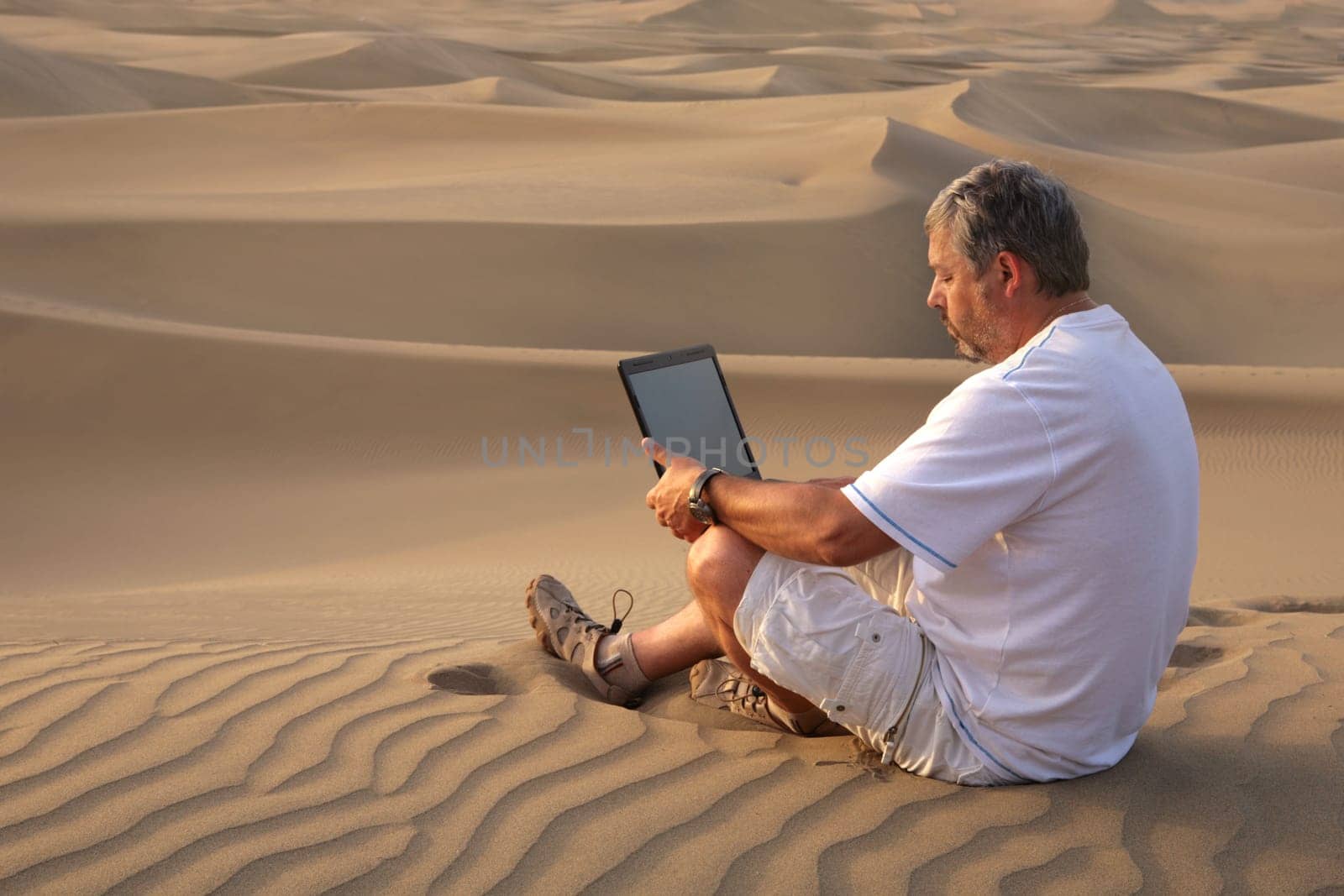 Man with laptop sitting in the desert.